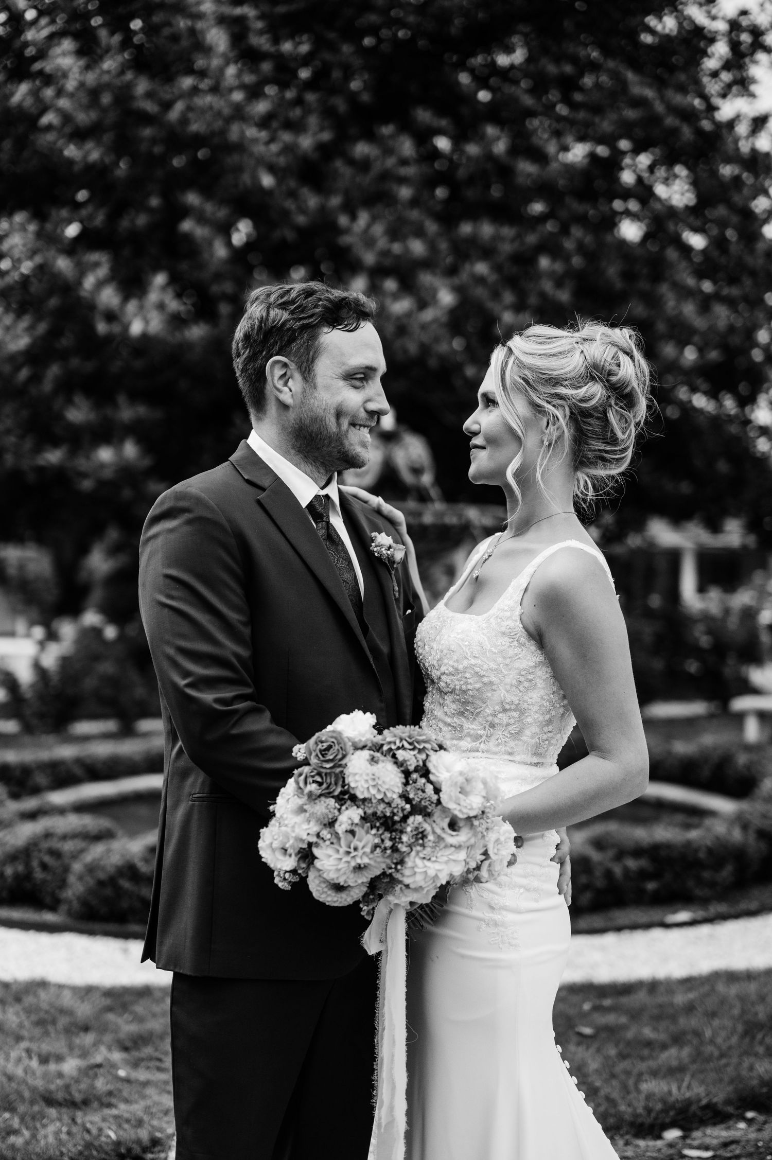 Black and white portrait of wedding couple sharing joyful moment in manicured garden.