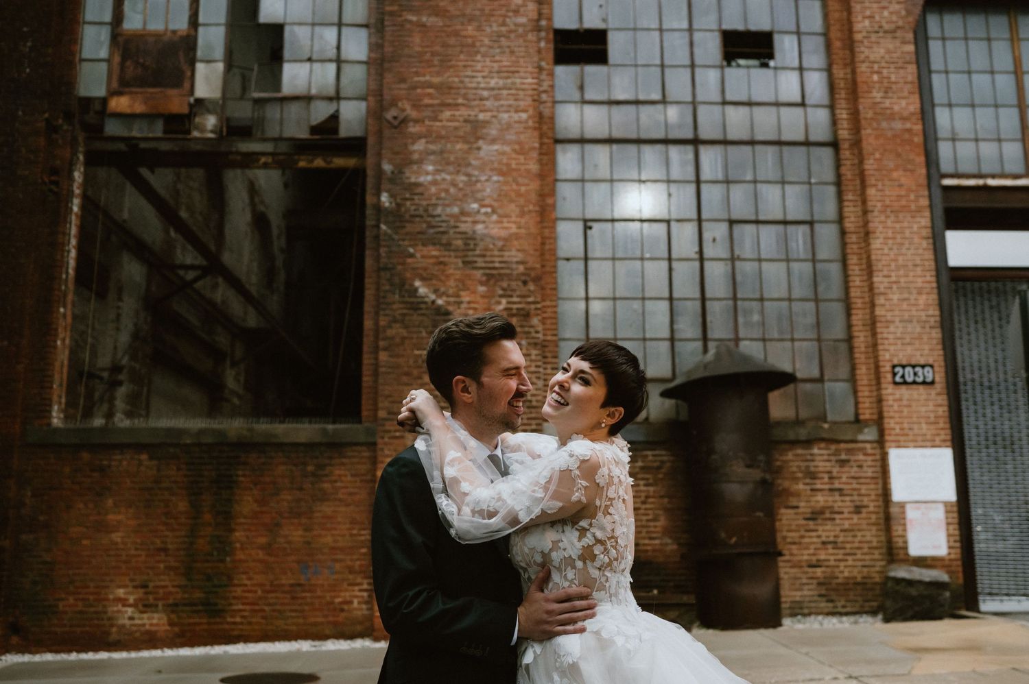 Newlyweds share an intimate moment together against a rustic brick wall backdrop.
