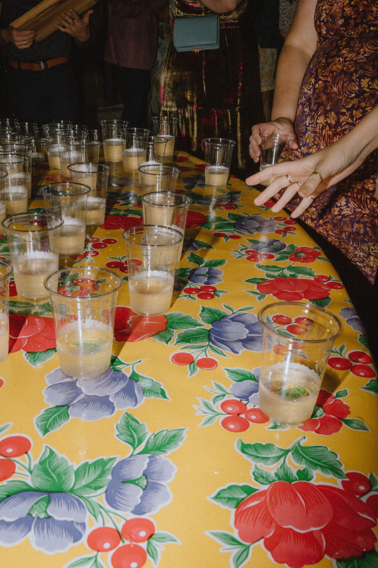 Rows of cocktail glasses on colorful floral tablecloth at wedding reception.