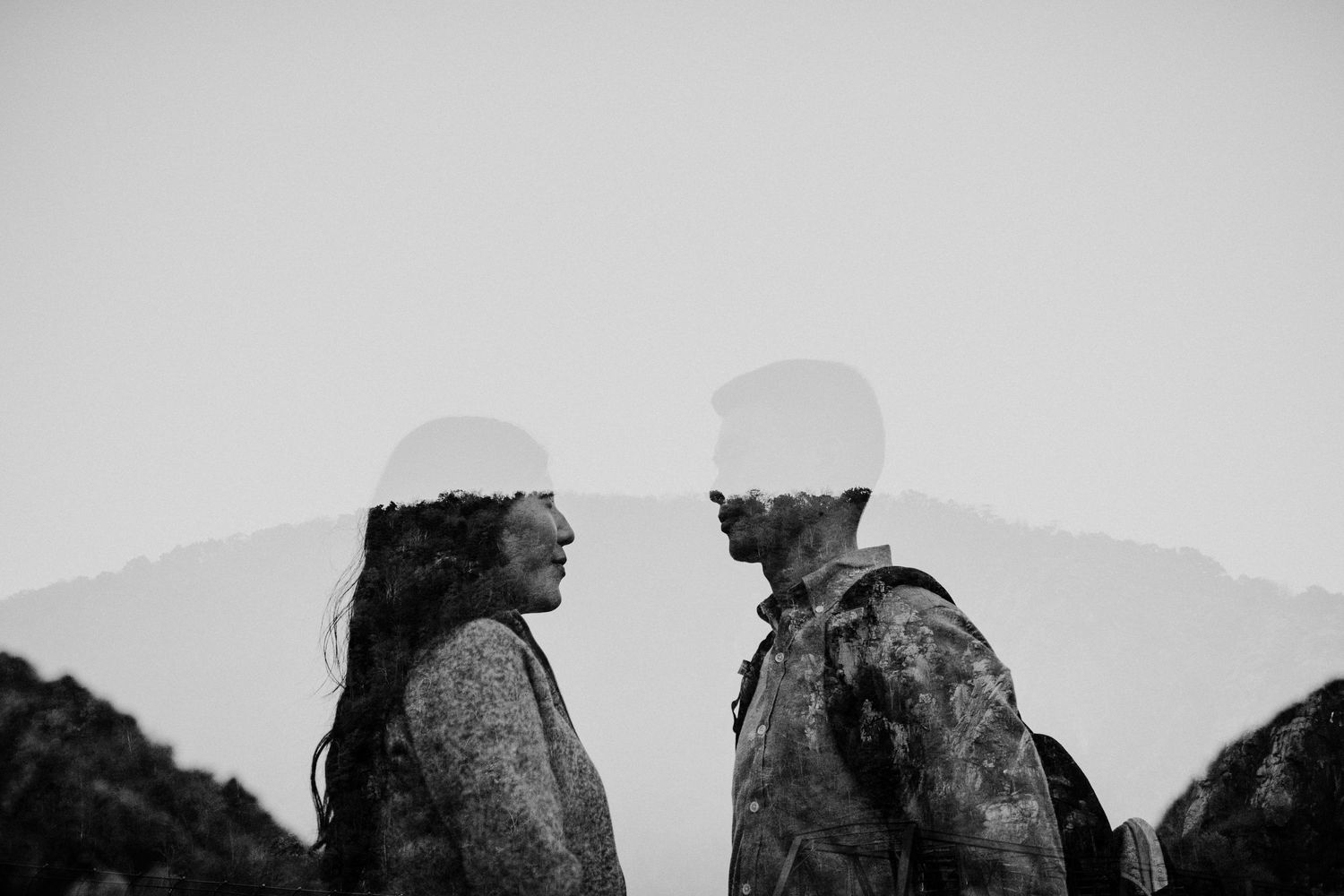 A silhouetted couple stands face to face against a misty mountain backdrop.