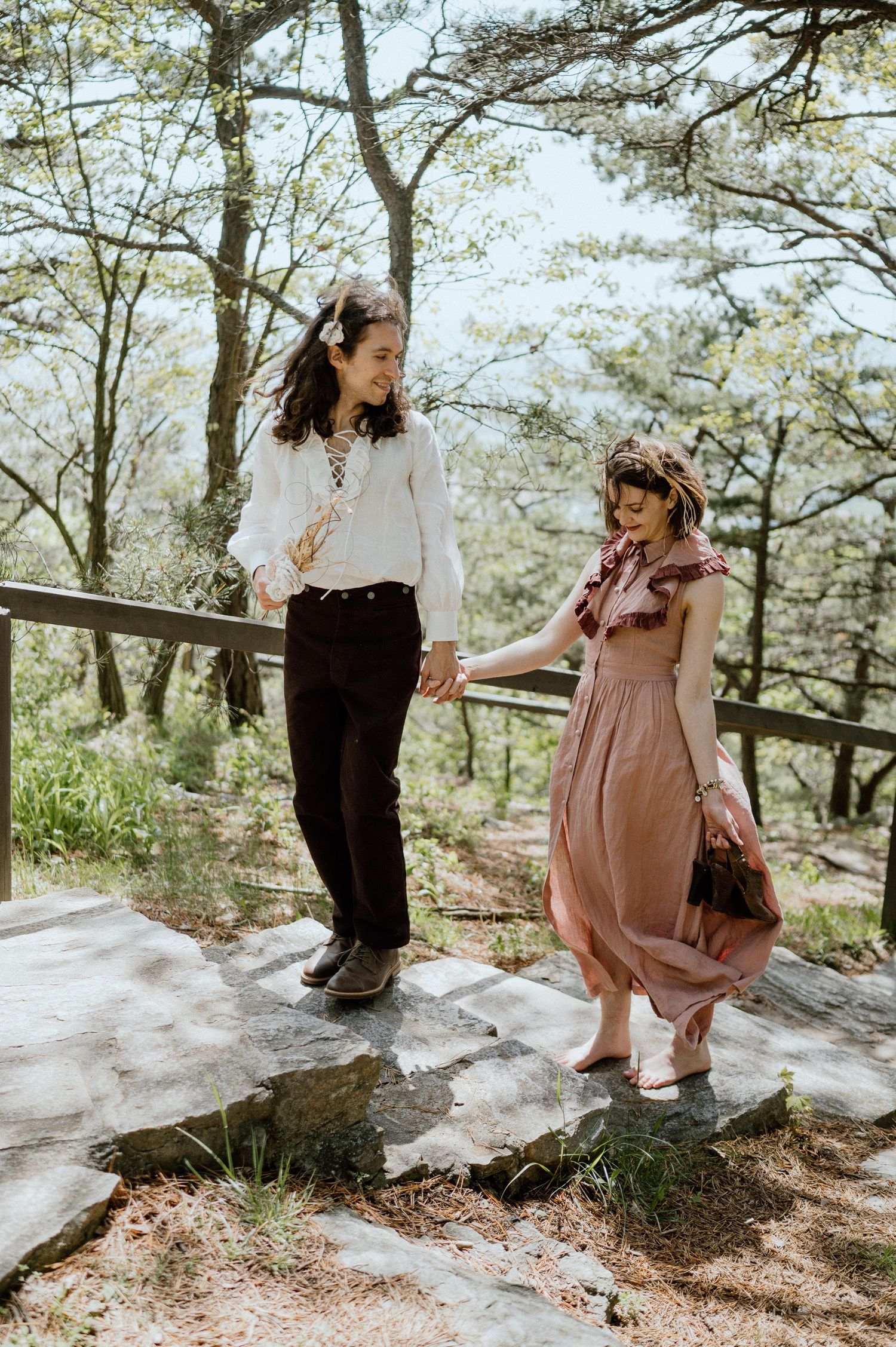 Two people walking along a scenic mountain path wearing contrasting vintage outfits in spring.