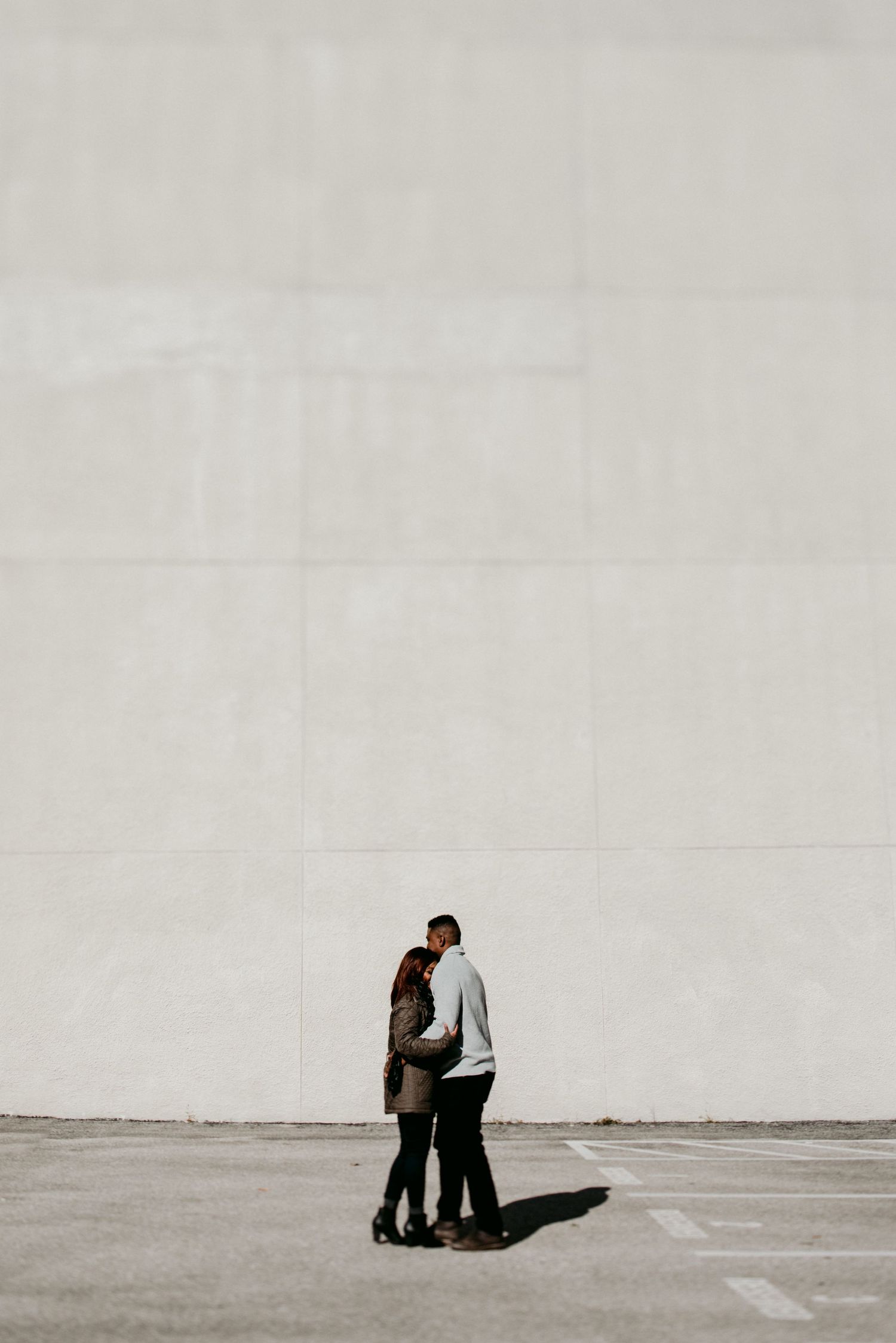 A couple embracing in silhouette against a minimalist white wall and concrete floor.