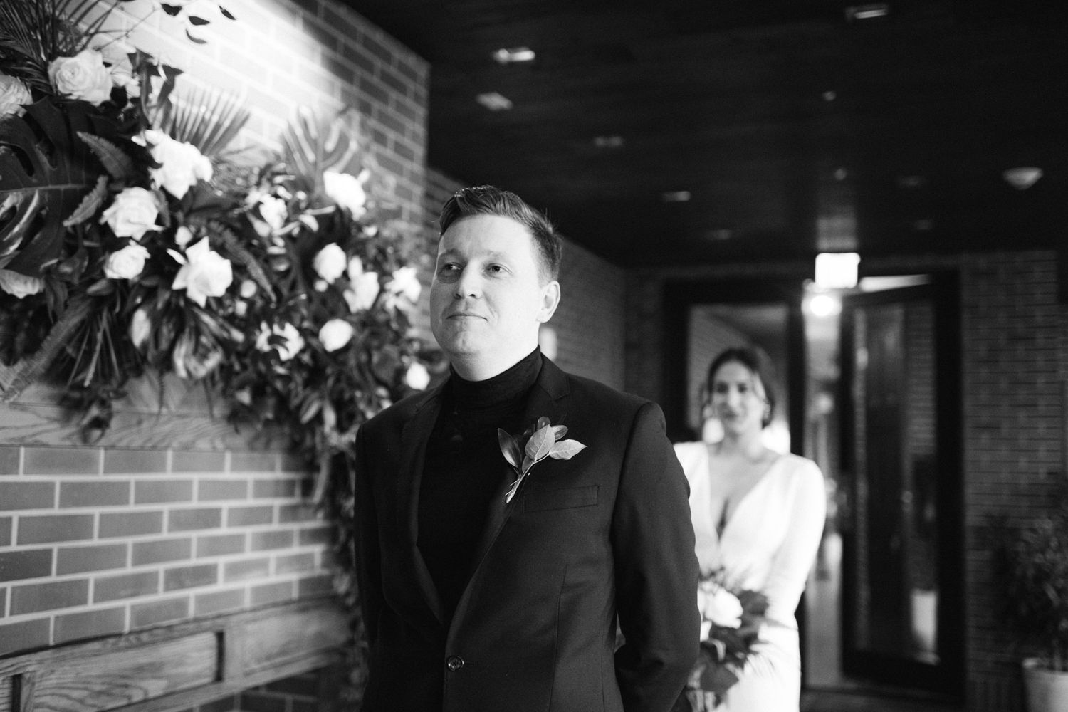 Romantic first look moment between couple against brick wall with floral arrangements.