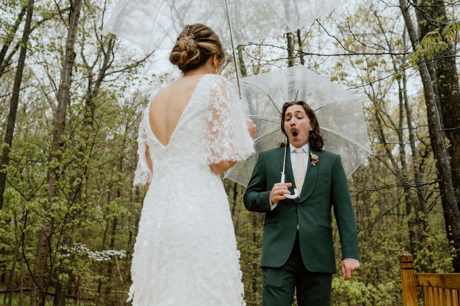 Couple shares first look moment on wooden deck during rainy forest wedding.