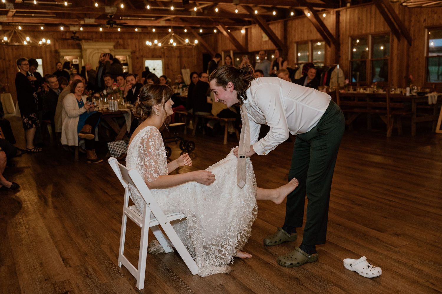 Wedding couple during traditional garter removal at reception on wooden dance floor.