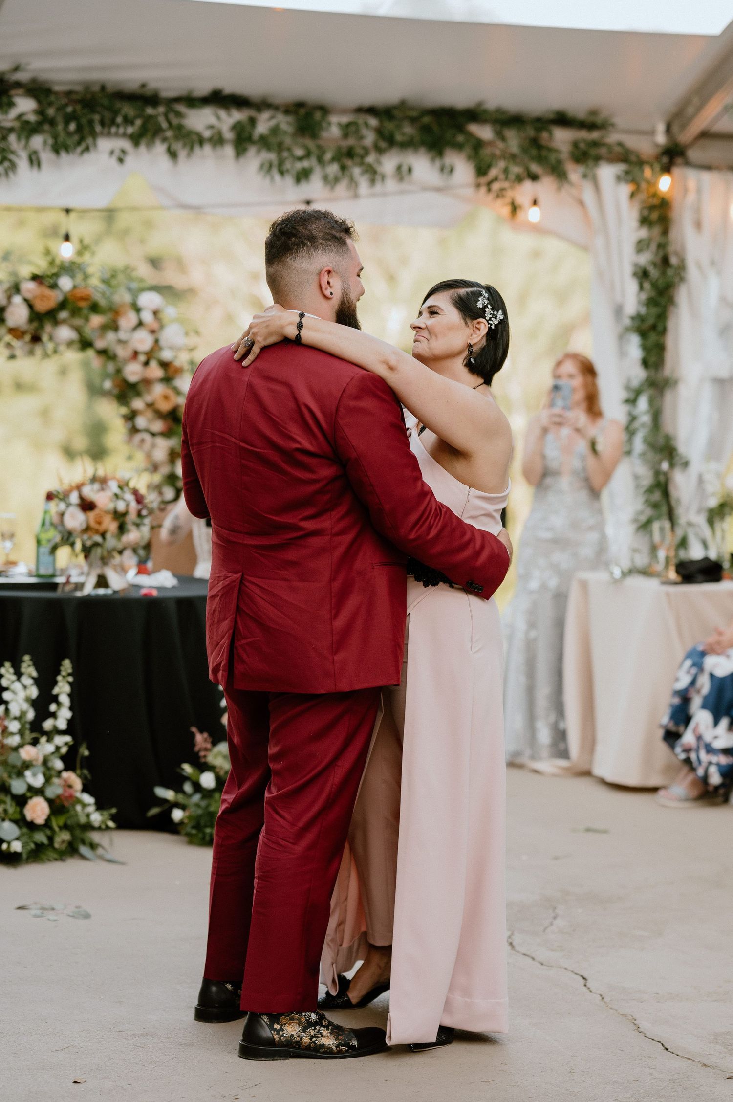 Couple shares intimate dance in burgundy and blush attire during outdoor wedding reception.