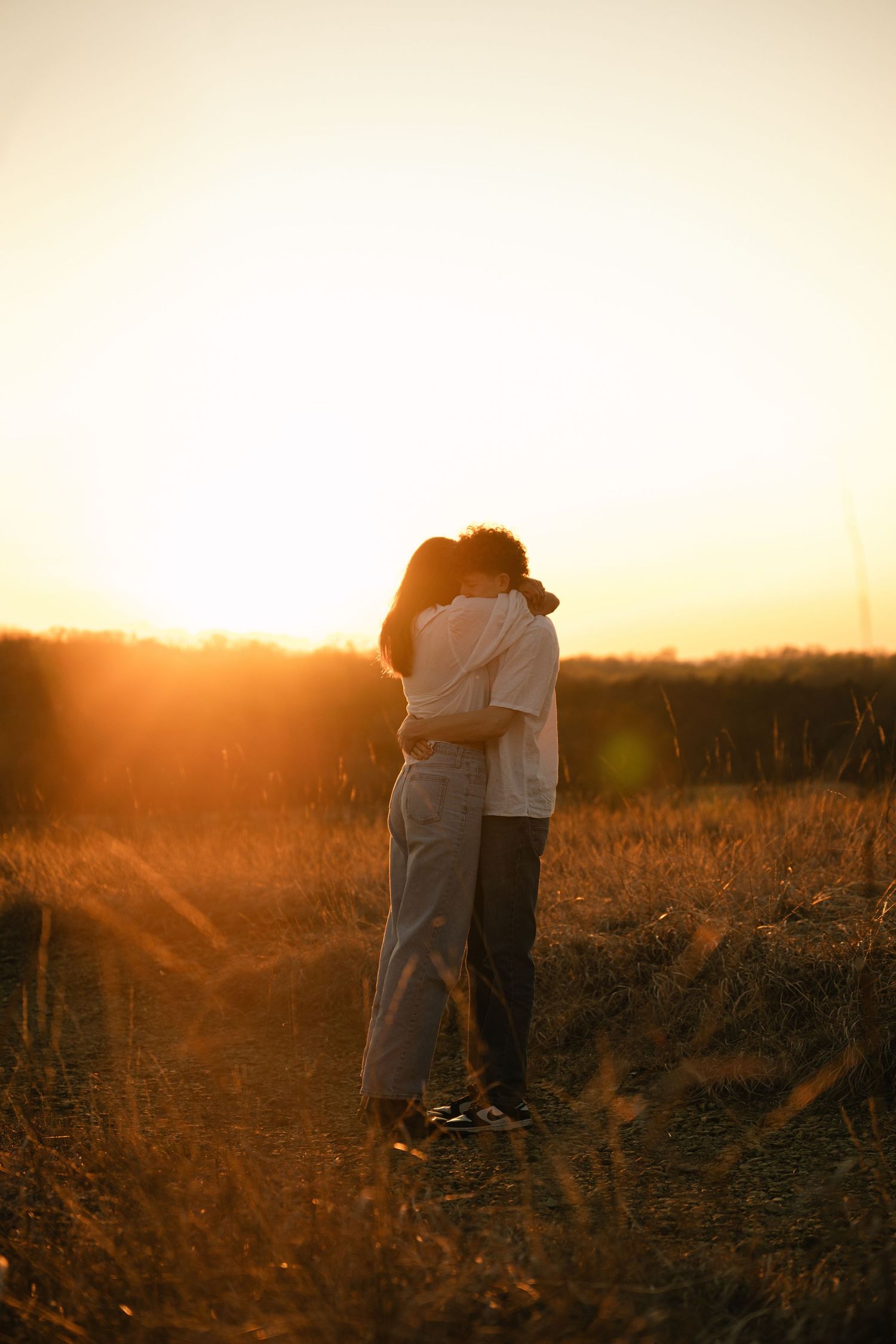 Couple embracing in golden sunset light in a field, silhouetted against warm glowing sky.