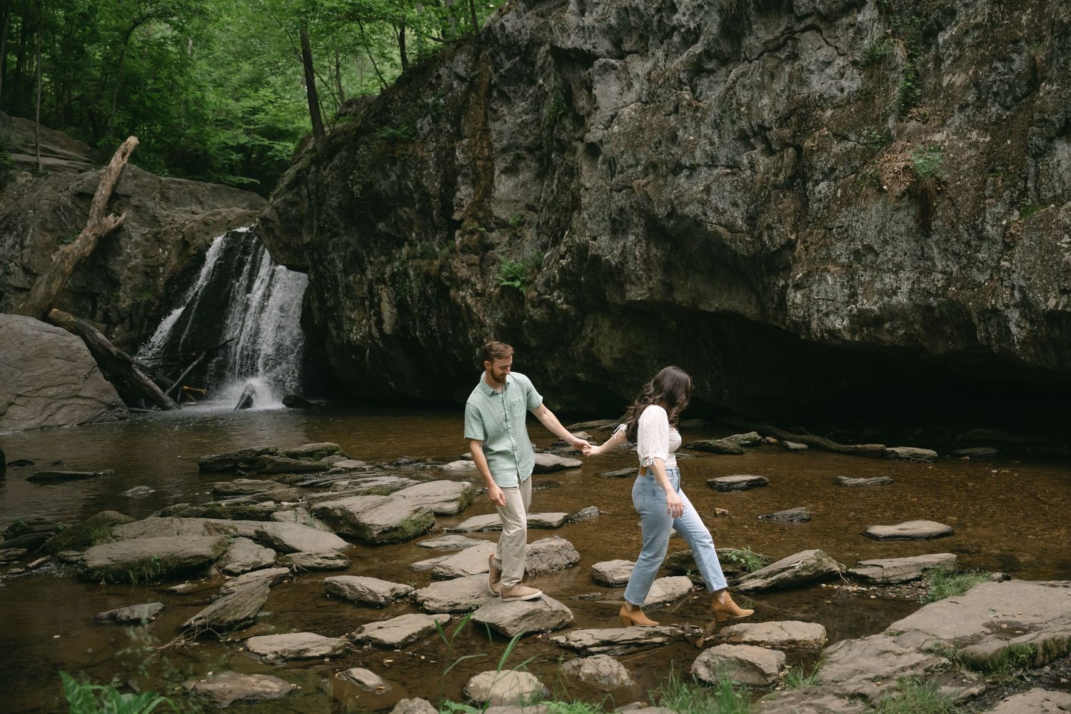 Stepping stones lead across a creek with a waterfall visible in the background.