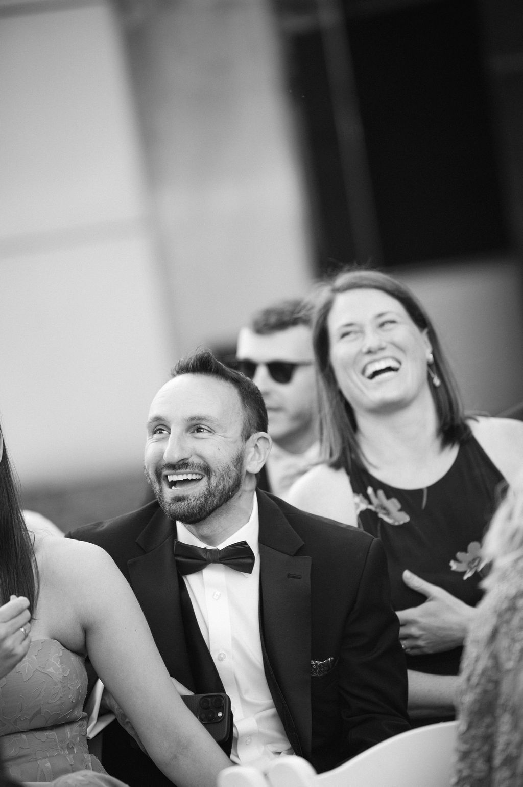 Black and white candid photo showing joyful laughter and reactions during a formal wedding reception.