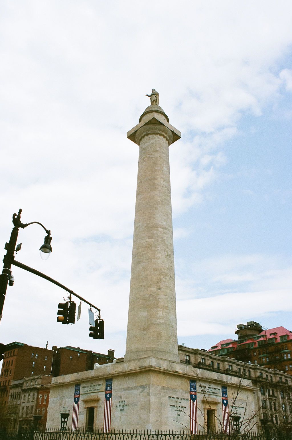 Historic white monument tower photographed against cloudy sky in urban setting.
