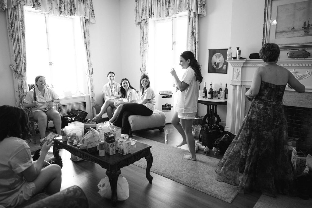 Black and white photograph of a gathering in a vintage-style living room with period furniture.