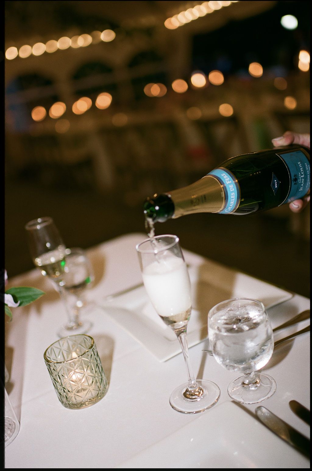 Wine being poured into glasses on a white tablecloth with bokeh lighting in the background.