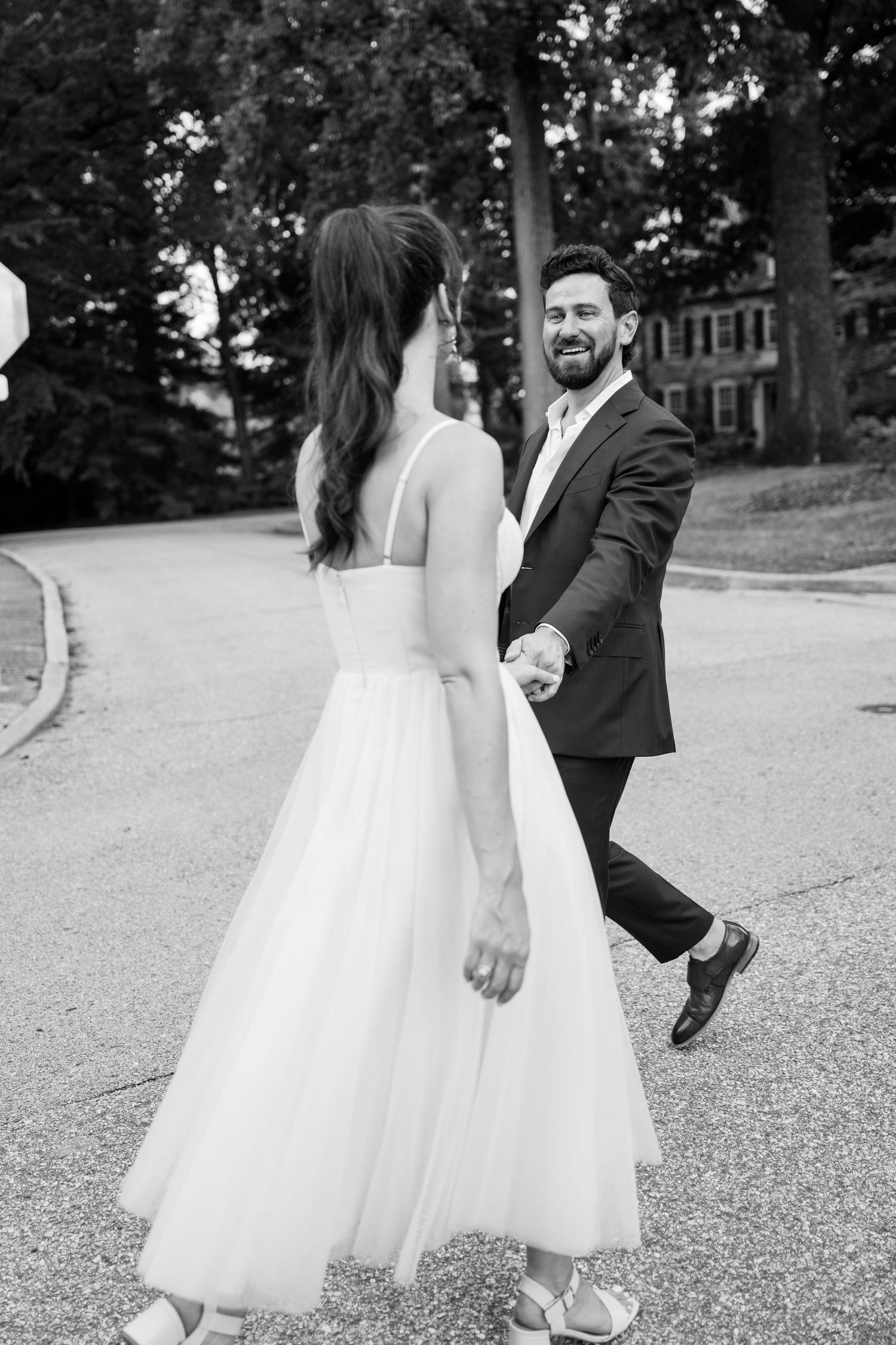 Black and white wedding photograph showing a couple playfully walking together on a gravel path.