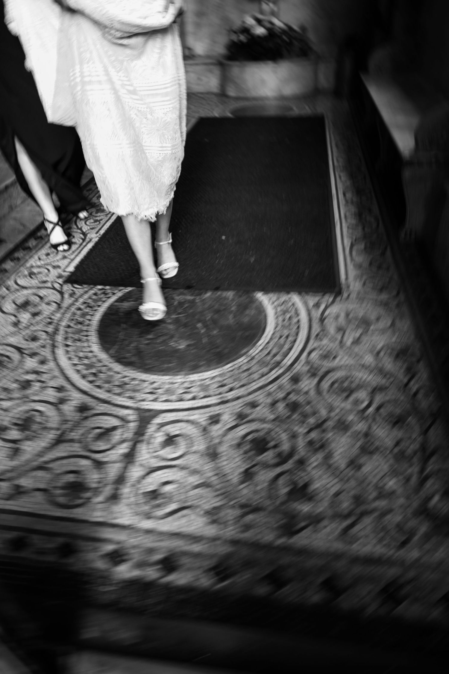Black and white photo of vintage shoes on ornate carpeted floor with circular pattern.