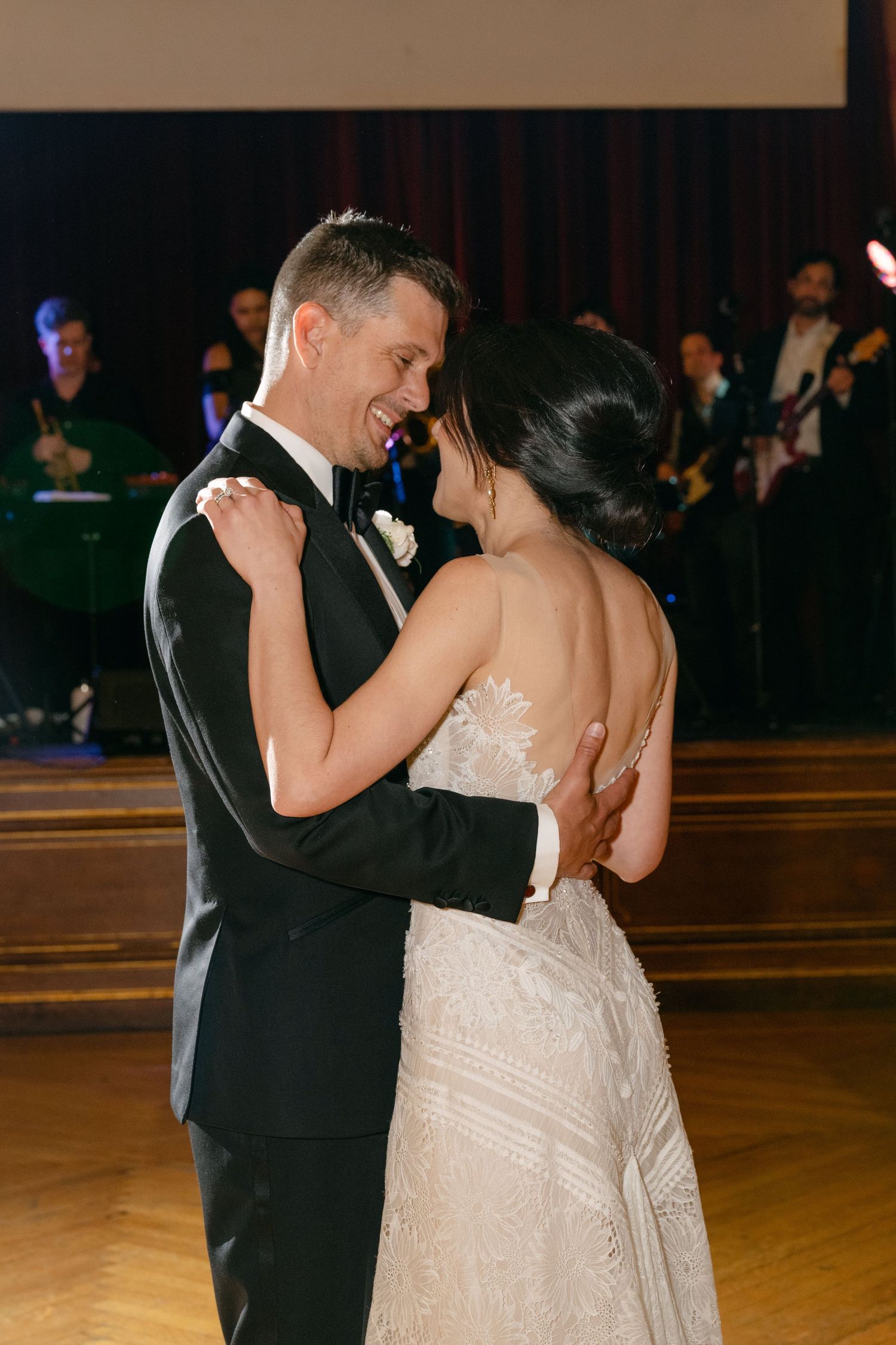 Newlyweds share their first dance on a polished wooden ballroom floor.