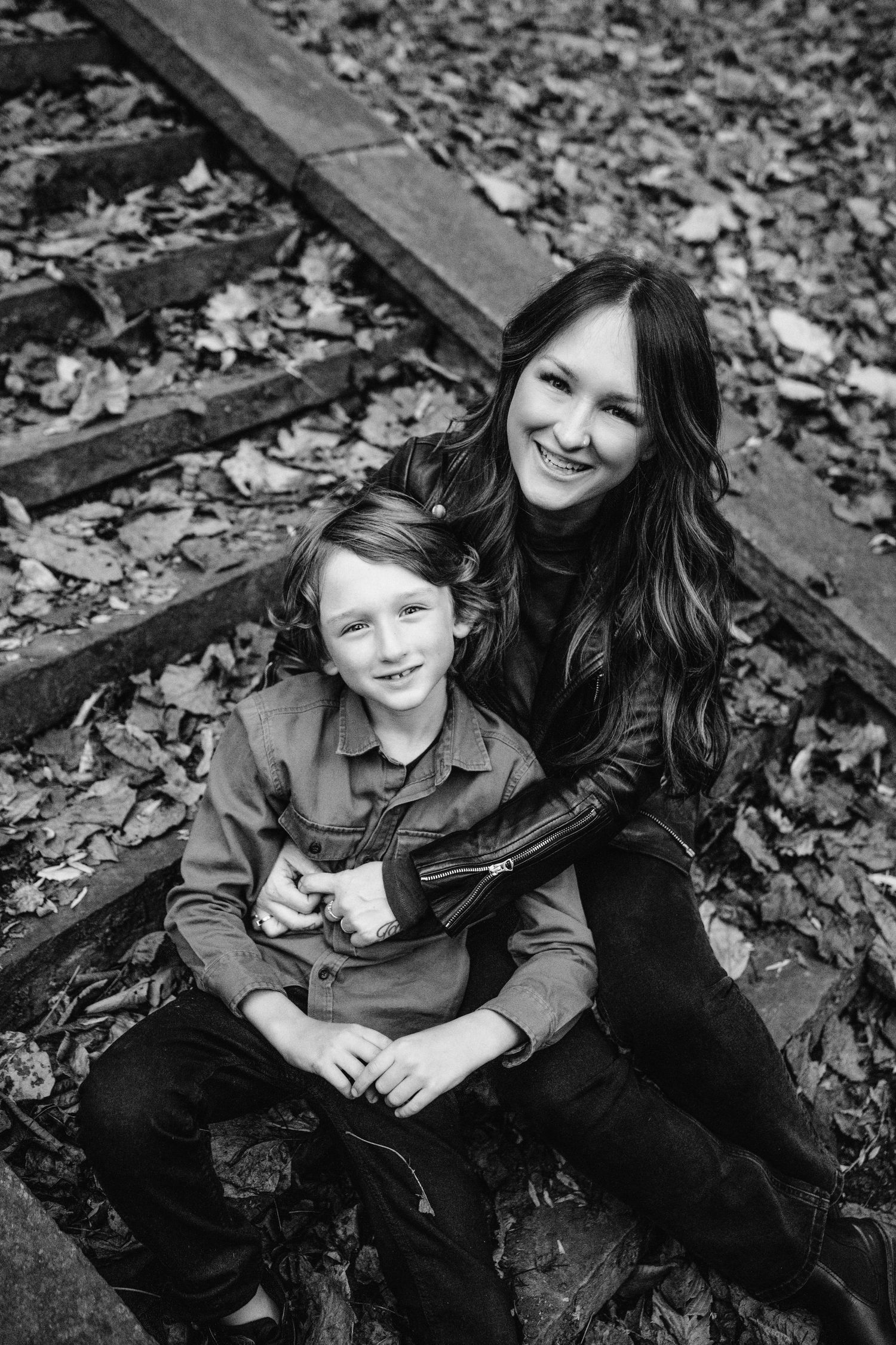 A black and white portrait capturing joy and connection on leaf-covered wooden steps.