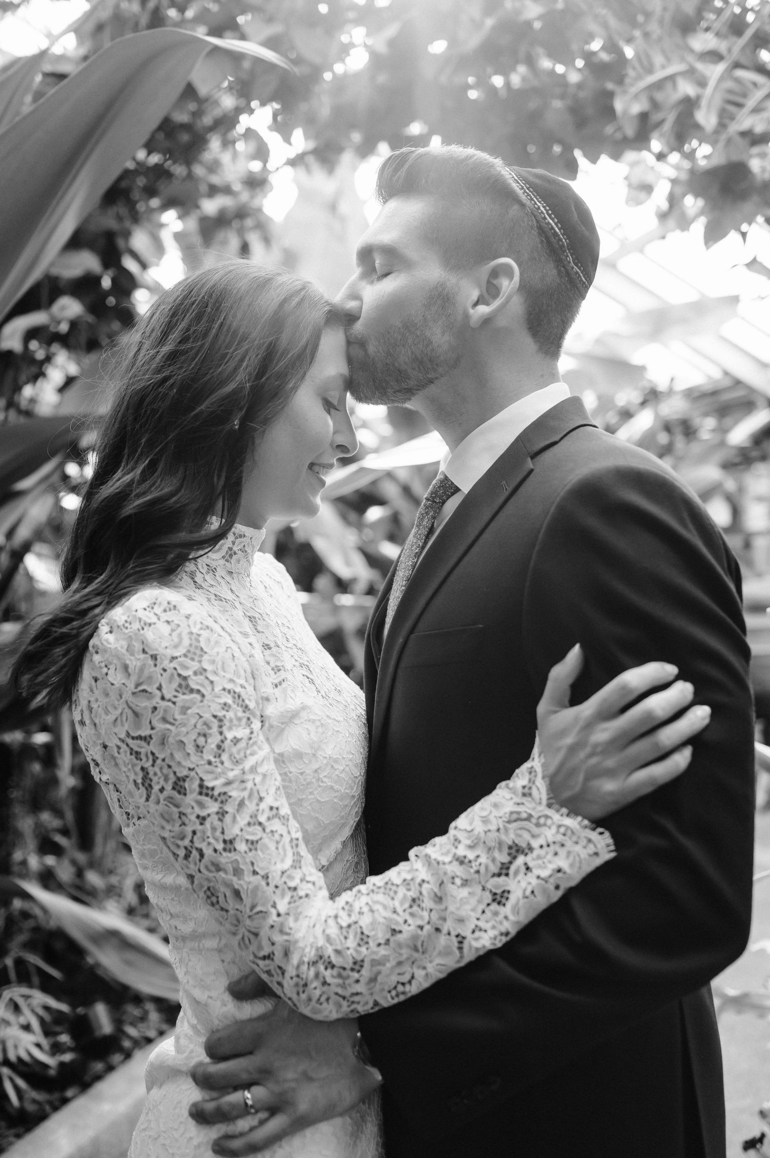 An intimate black and white portrait of a romantic embrace in a garden setting.
