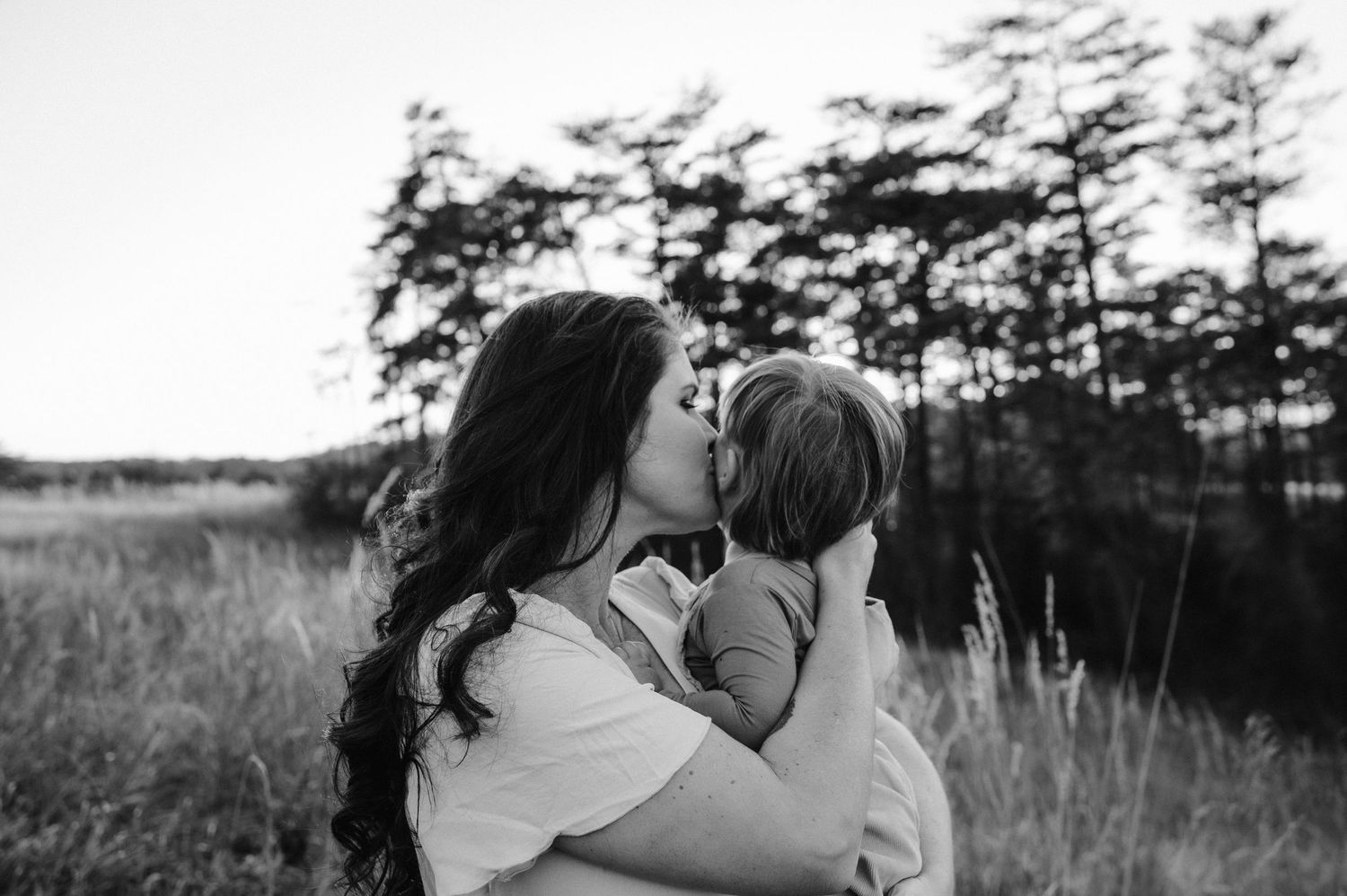 Black and white intimate portrait of tender family moment in a grassy field.