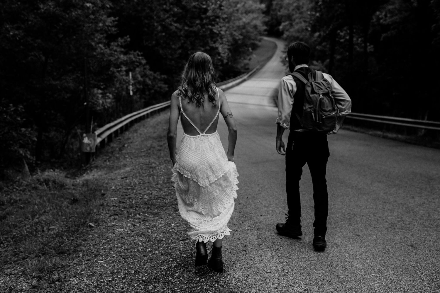 Black and white photo of two people with backpacks walking on a winding forest road together.