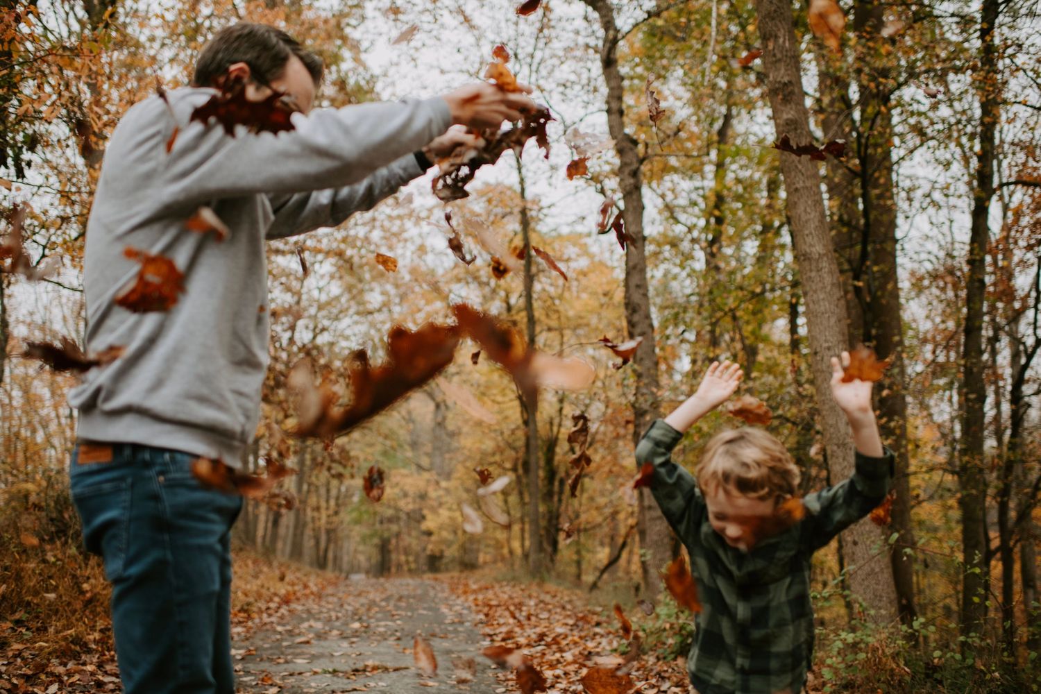 People playing with autumn leaves in a forest on a fall day.