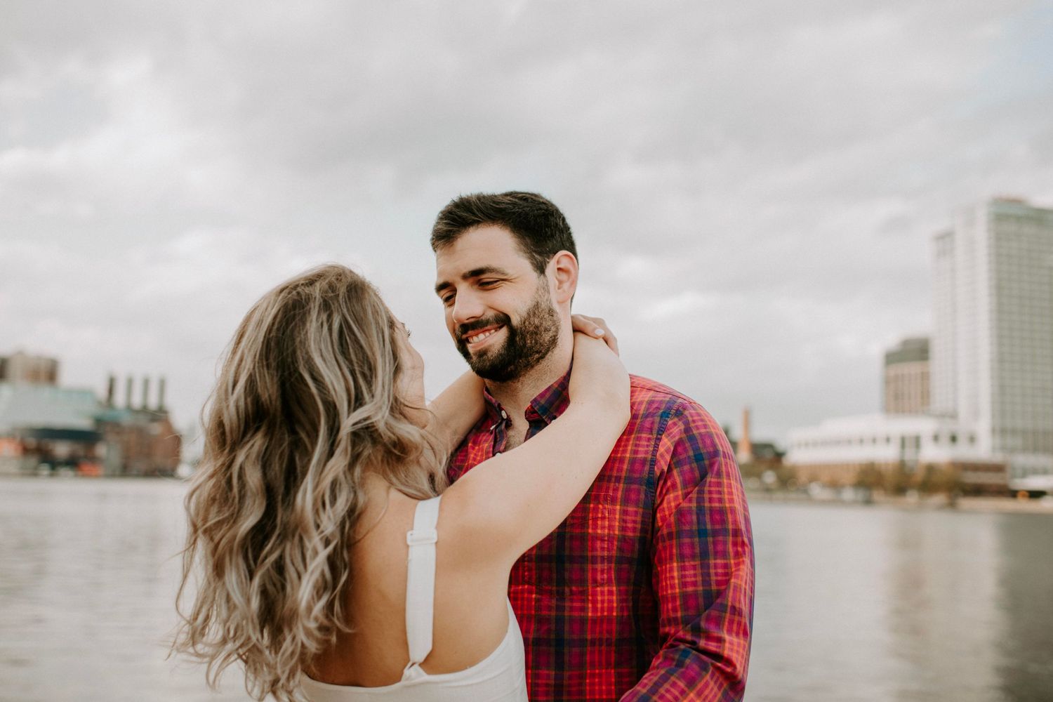 Romantic moment captured by waterfront with urban skyline backdrop.