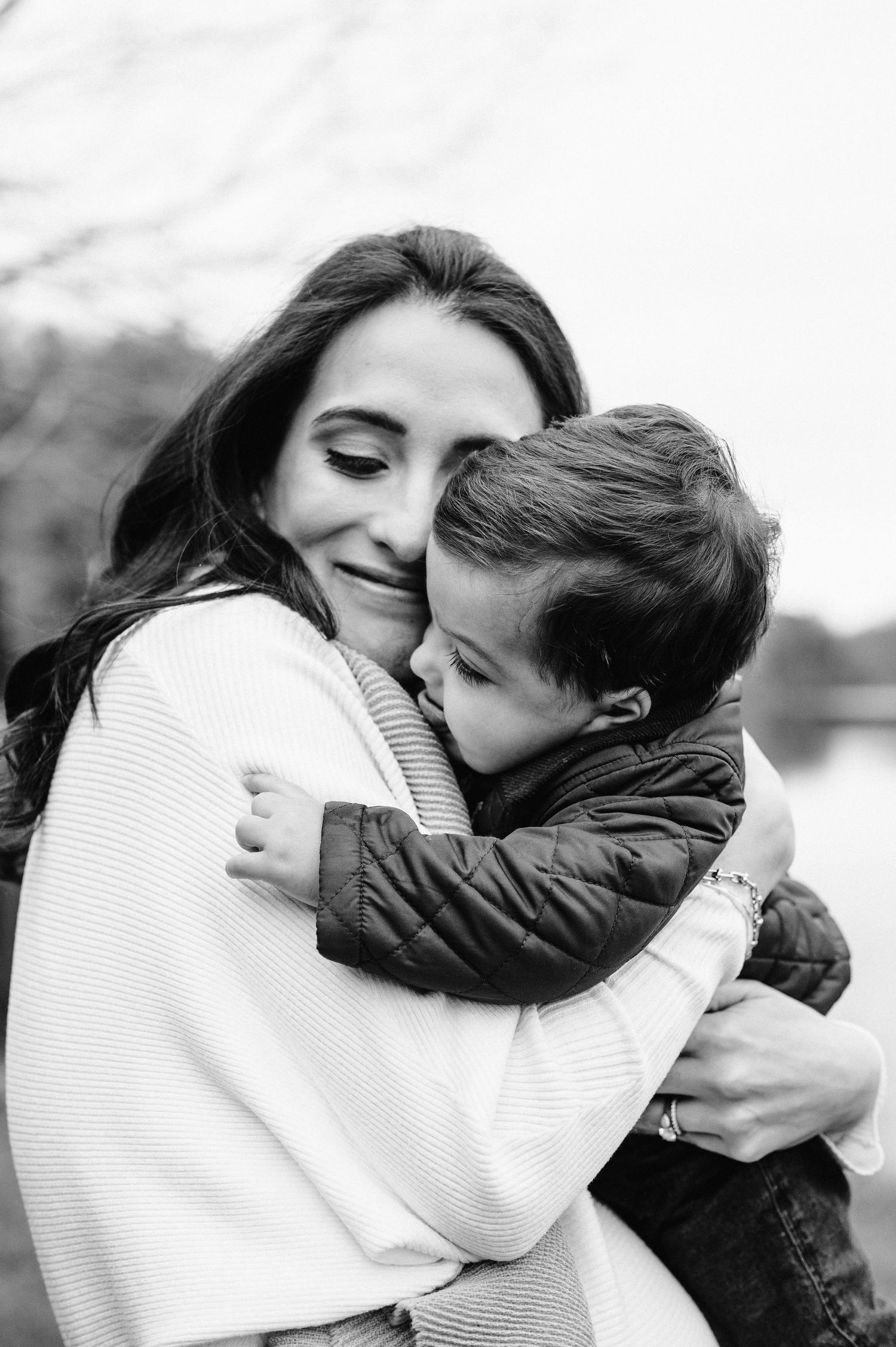 Black and white portrait of tender embrace between parent and child outdoors.