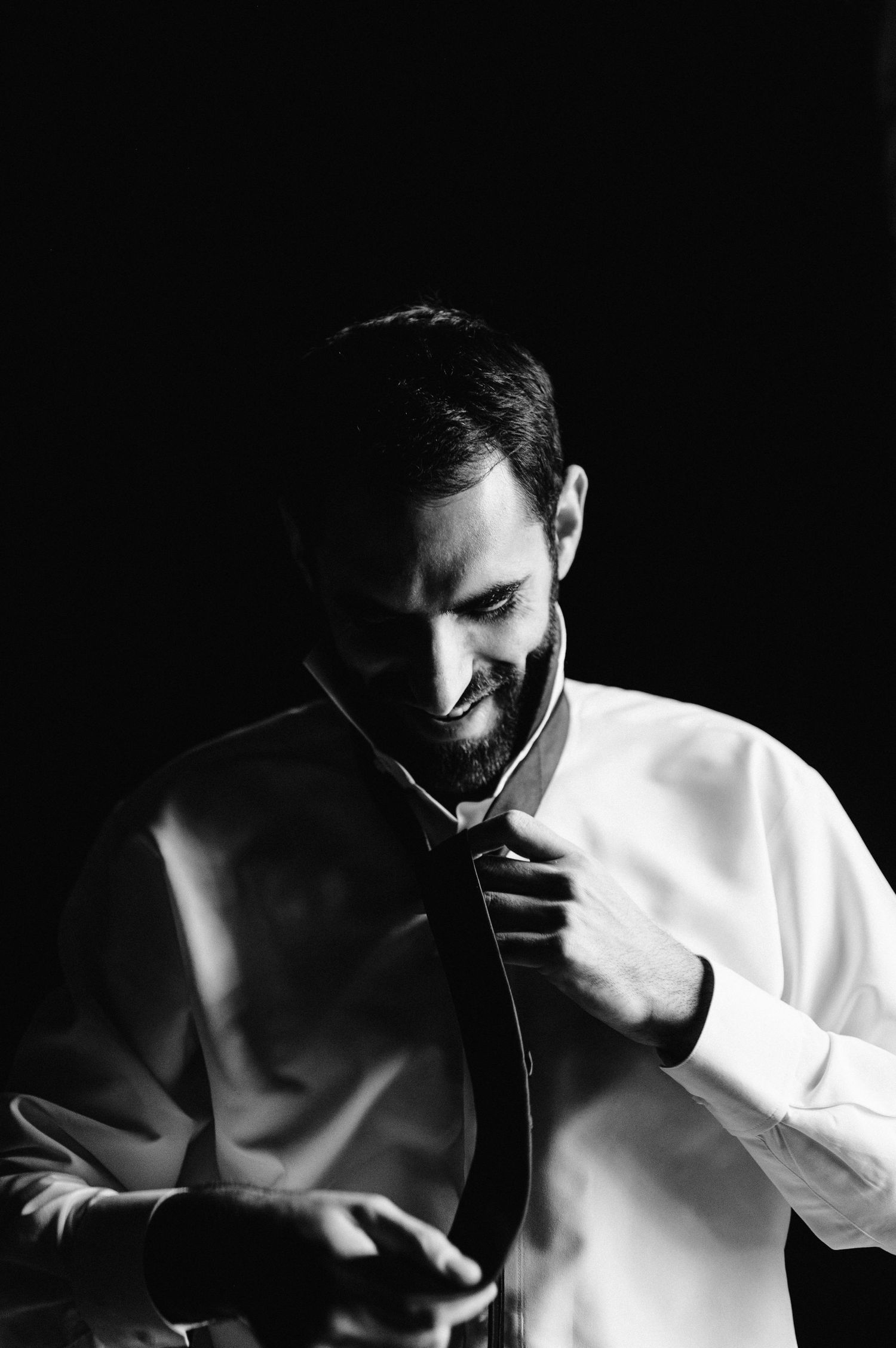 High contrast black and white image of someone adjusting a tie with dramatic lighting.