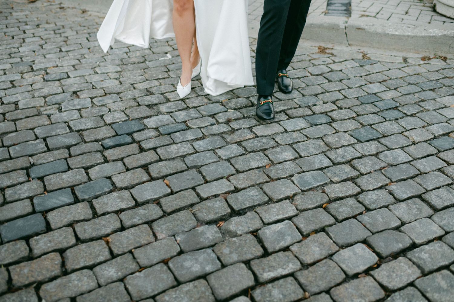 Close-up of wedding couple's feet walking on cobblestone street.