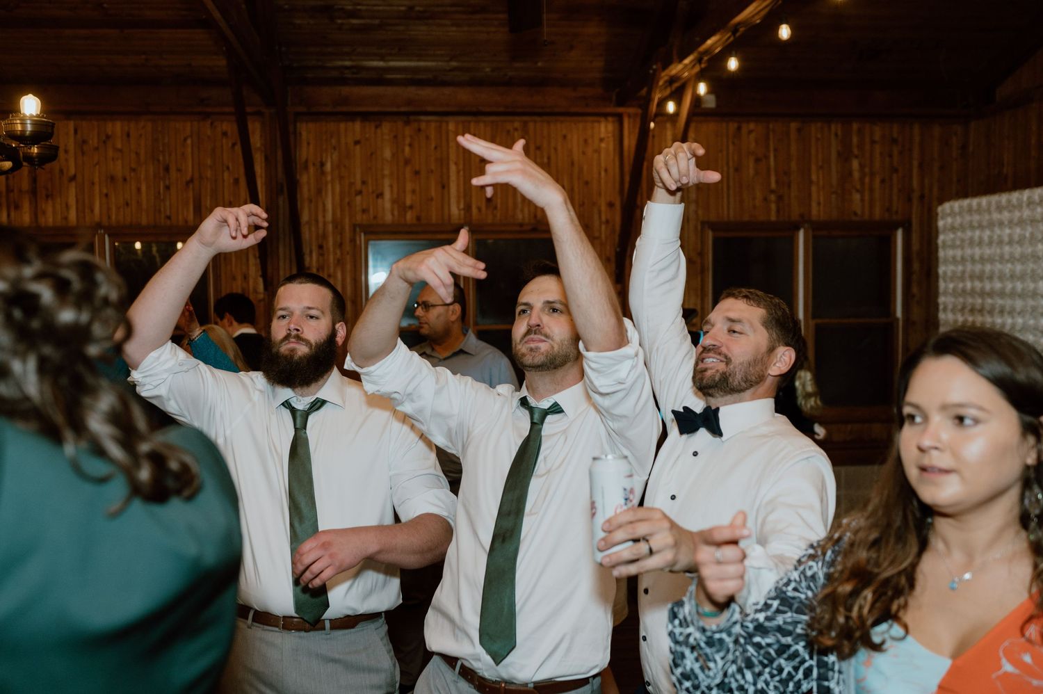 Wedding guests dancing and celebrating with raised arms in a rustic wooden venue.