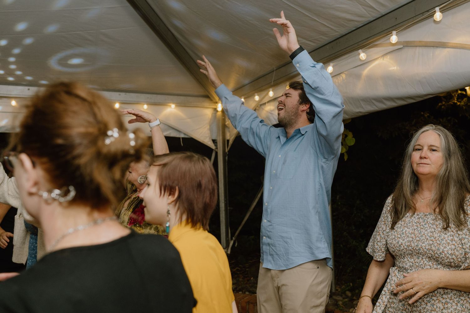 Guests dancing and celebrating at an evening event under a tent with atmospheric lighting.