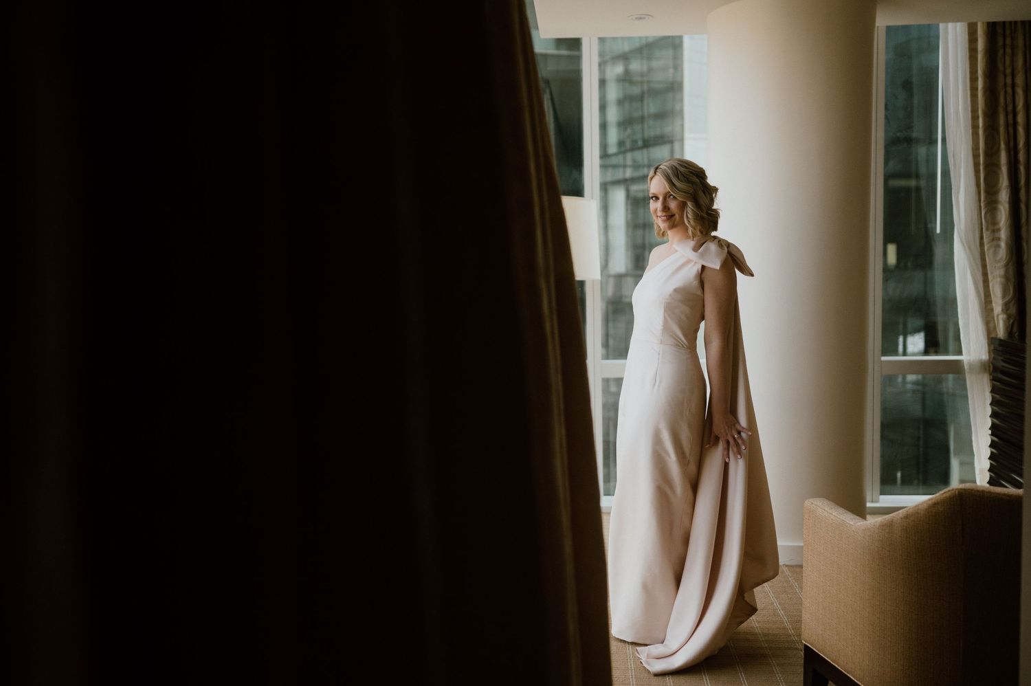 Silhouetted figure in flowing dress stands by window in morning light.