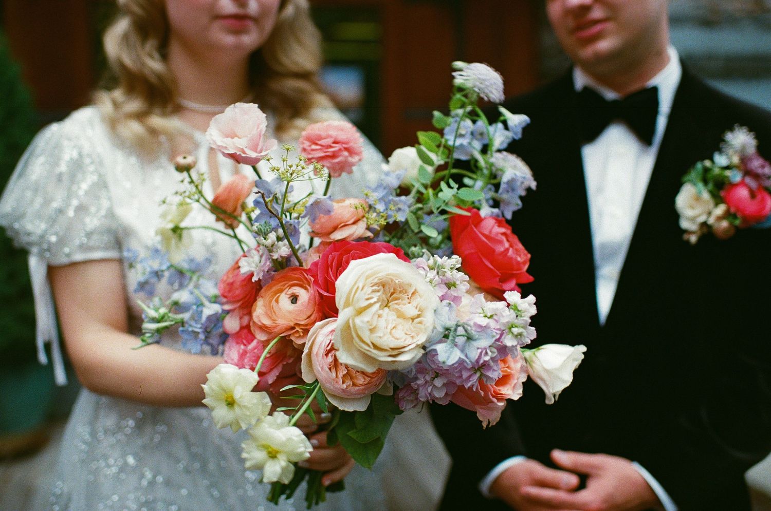 A beautiful wedding bouquet features coral, peach and blue flowers against formal attire.