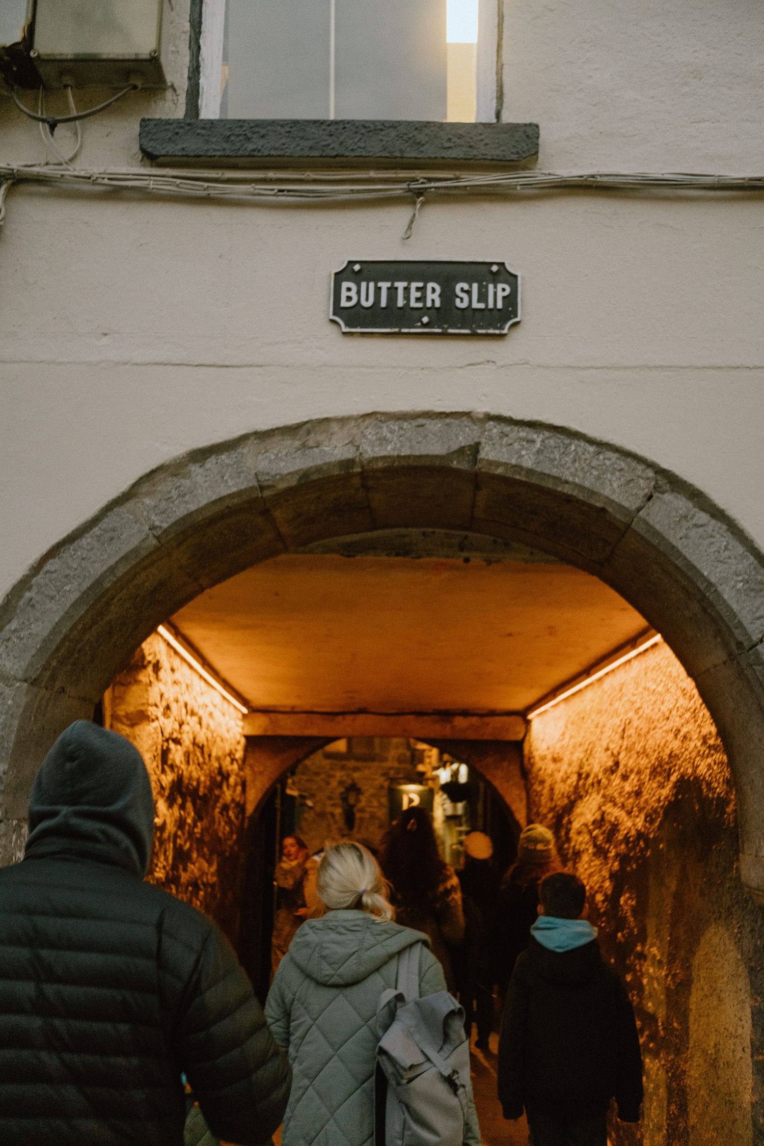 Visitors entering the Butter Slip, a historic medieval passageway with stone walls.