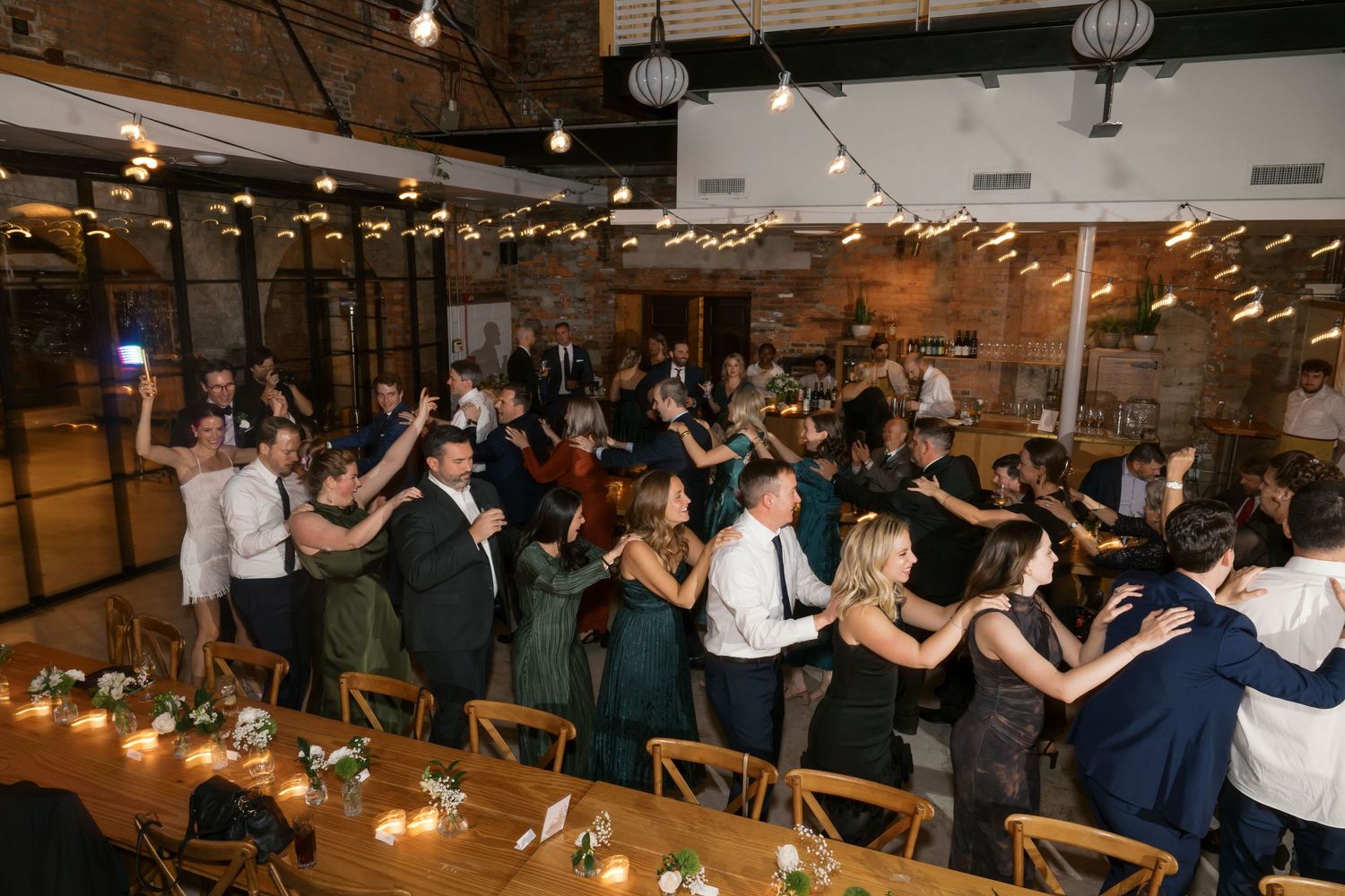 Wedding reception guests performing a coordinated group dance in an industrial-style venue.