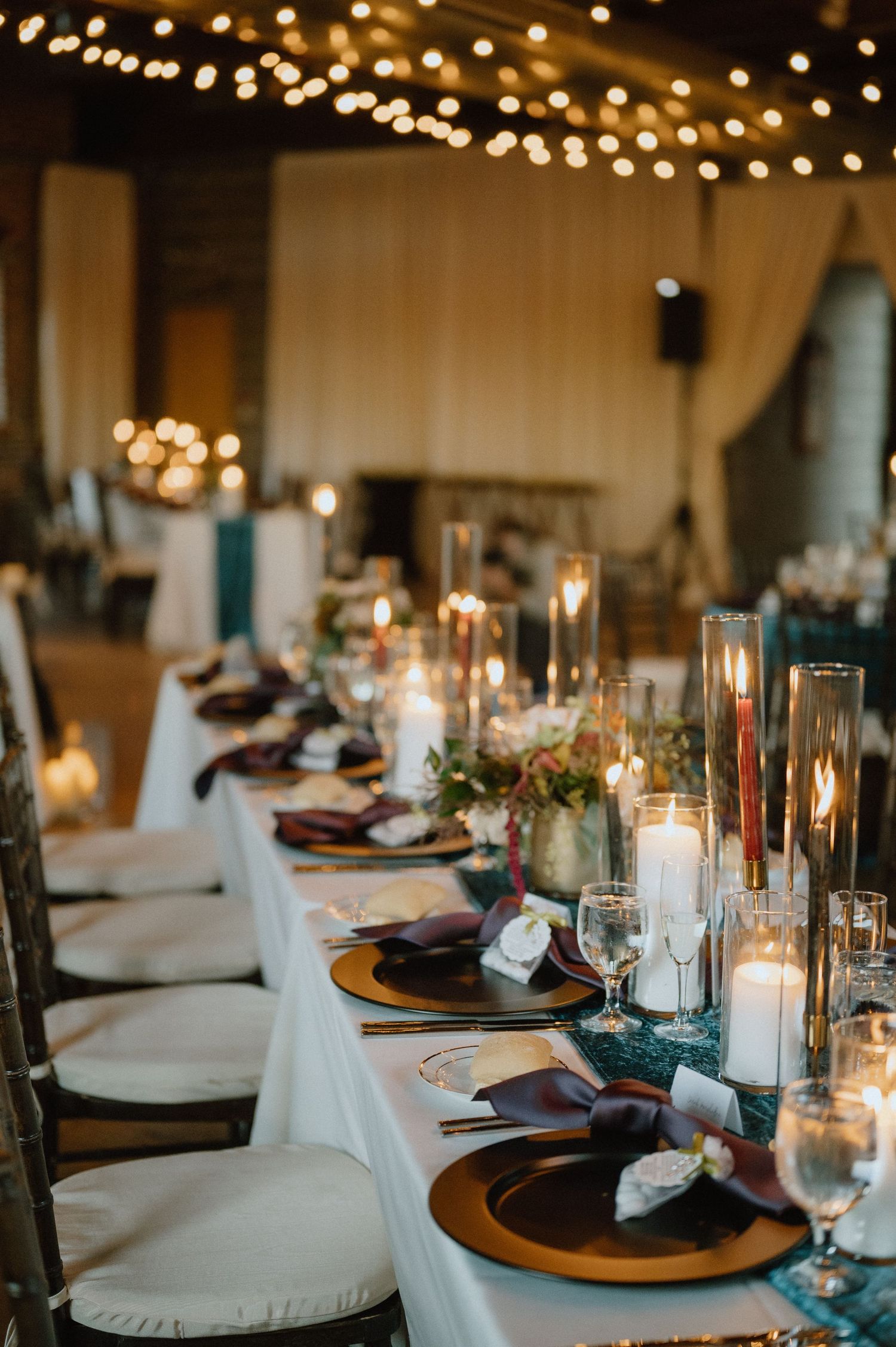 An elegant wedding reception table setting with glowing candles and string lights creating romantic ambiance.