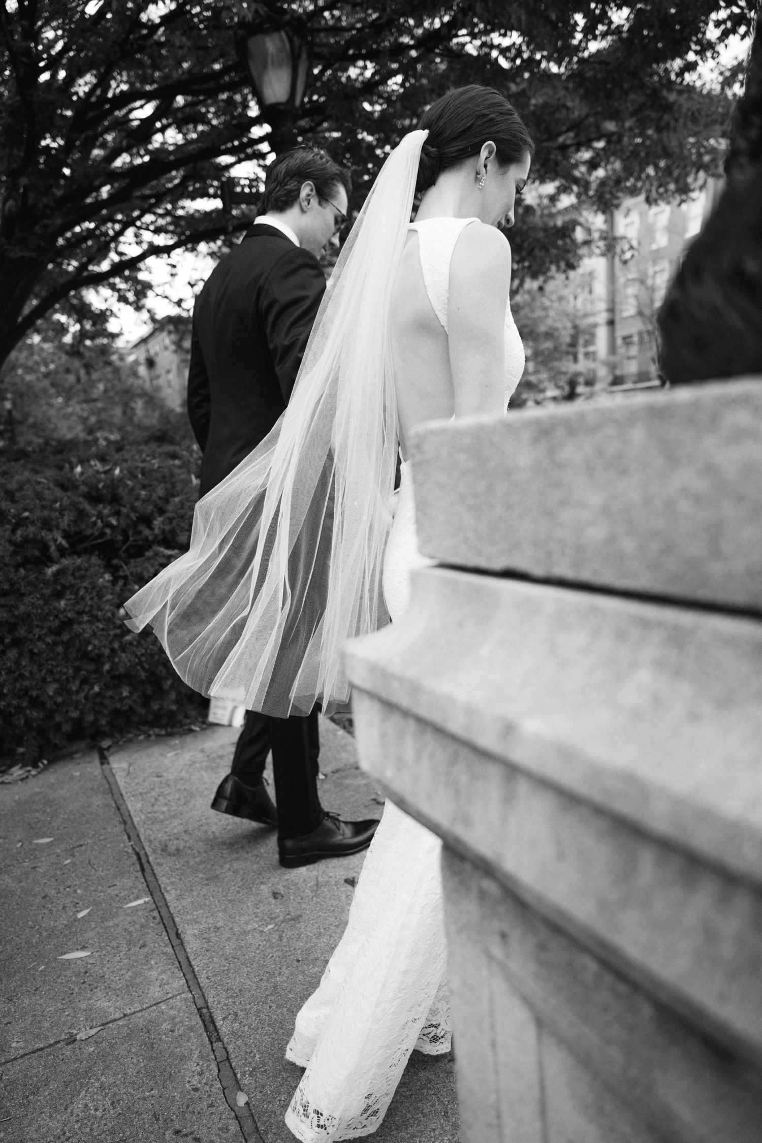 Black and white photo of couple ascending stone steps with flowing bridal veil.