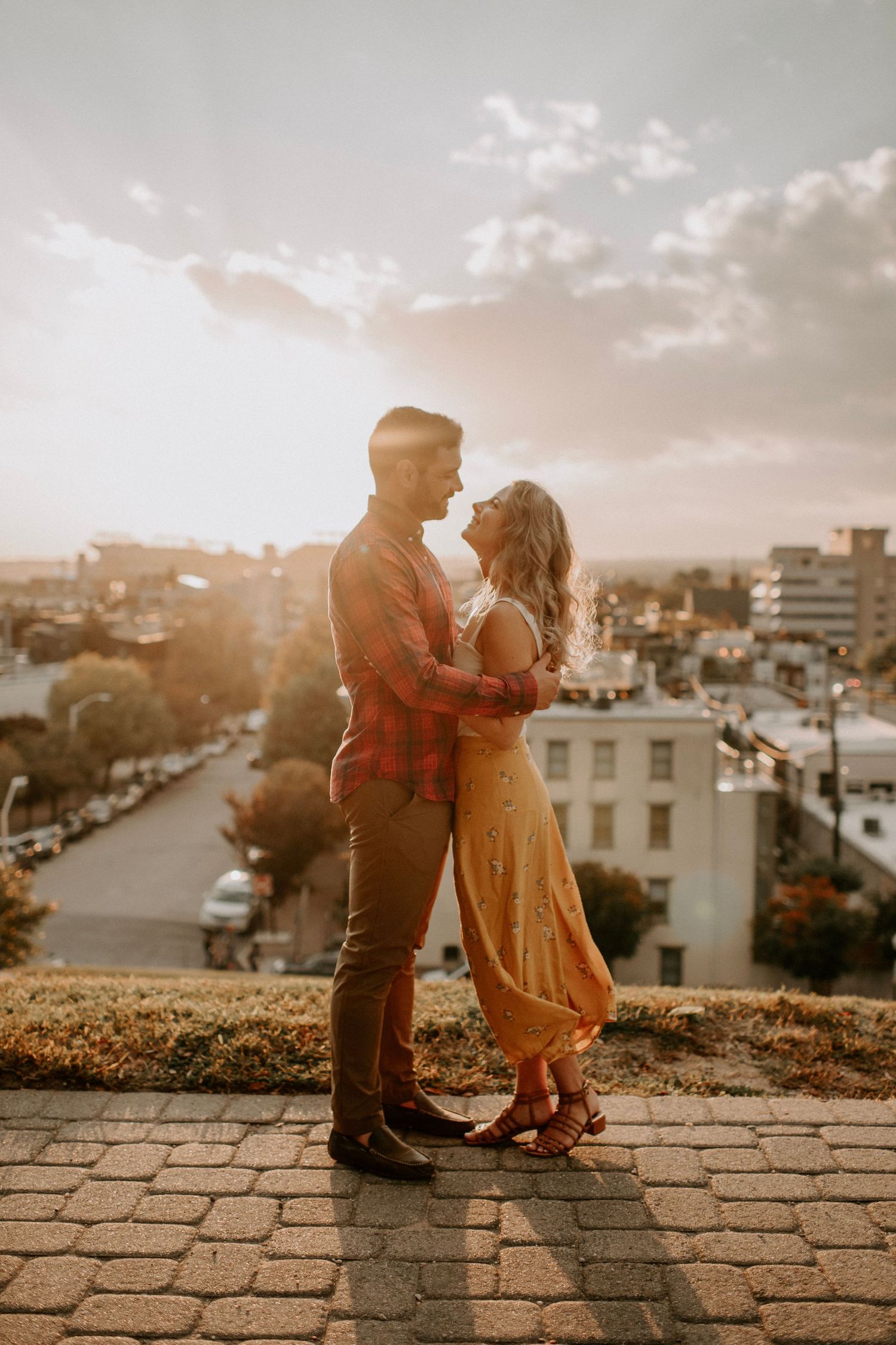 Couple embracing at golden hour on a rooftop overlook with a city skyline backdrop at sunset.