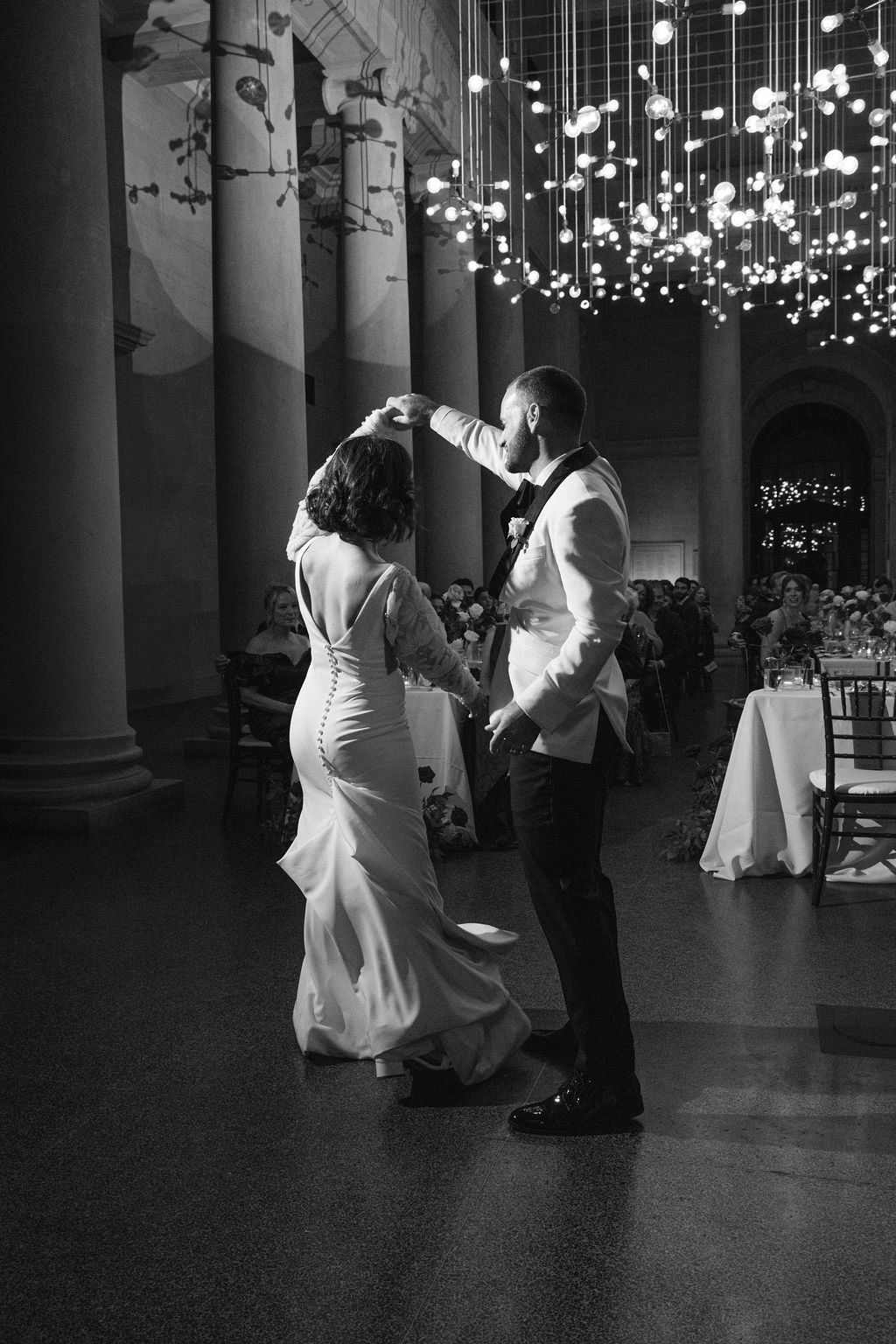 A romantic wedding dance sequence captured in black and white under twinkling lights and elegant columns.