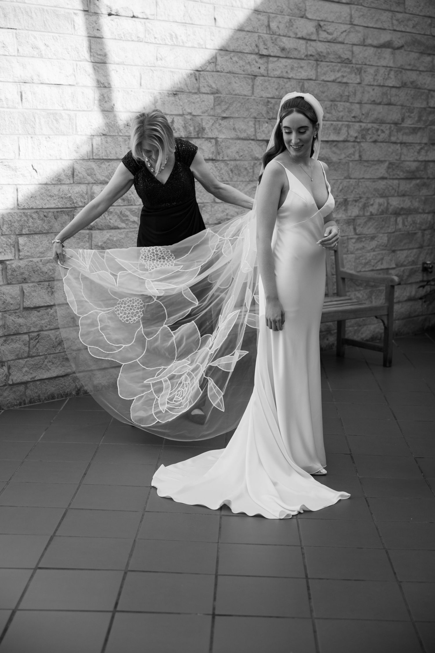 Elegant wedding dress with flowing veil captured in dramatic black and white against a stone wall.