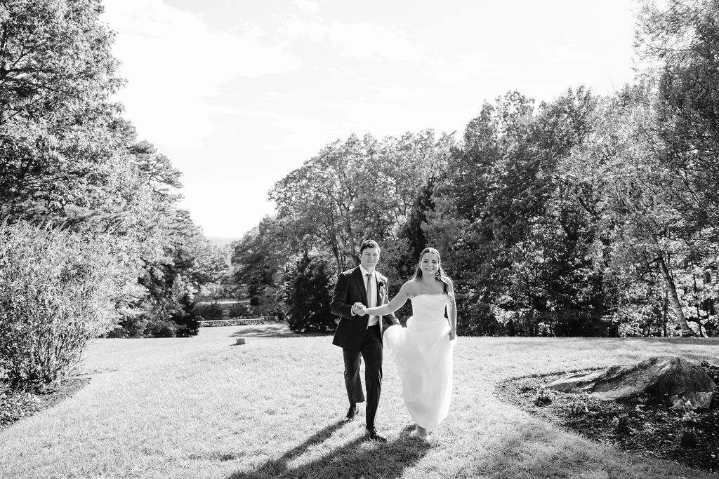 A couple walks along a tree-lined path in black and white wedding photography at Strong Mansion on Sugarloaf Mountain