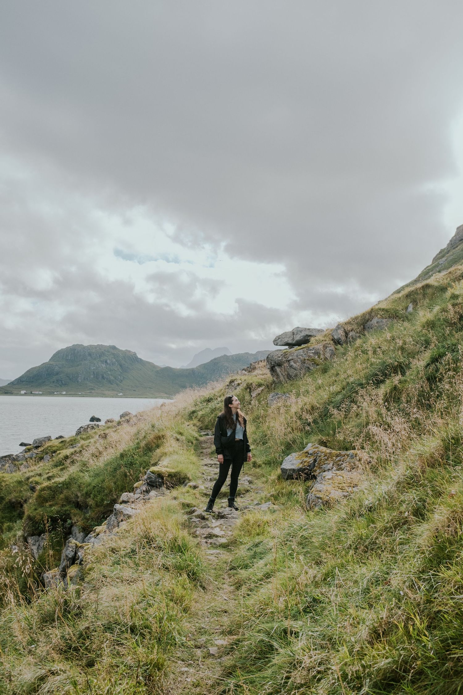 Hiker on coastal trail overlooking dramatic mountain and sea views in Nordic landscape.