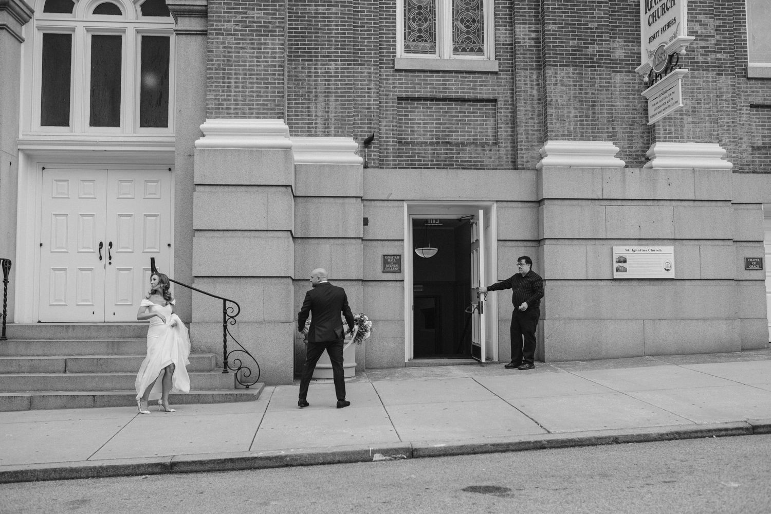 Black and white photo of people entering a brick church building with white trim.