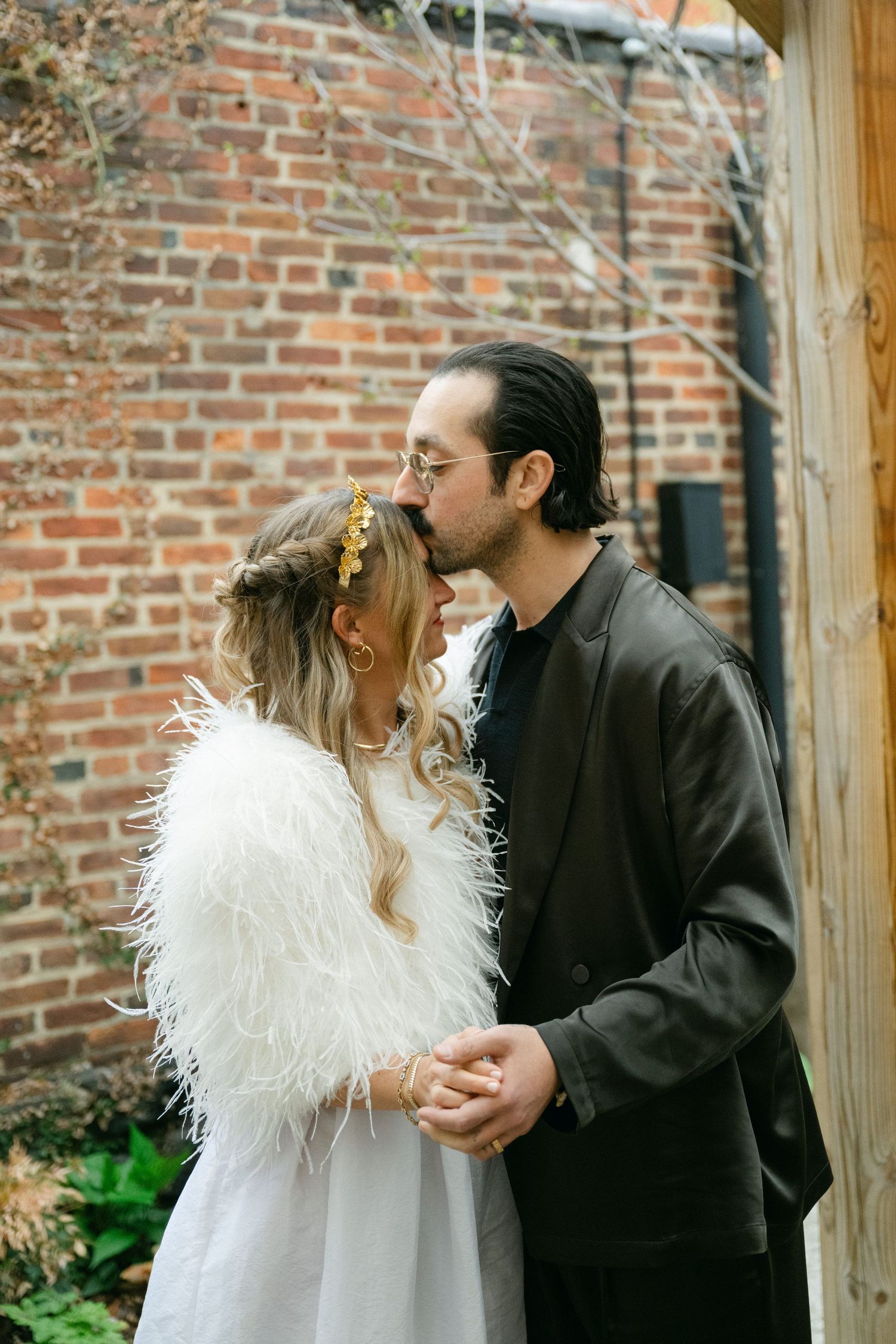 A couple in wedding attire sharing a romantic moment against a brick wall.