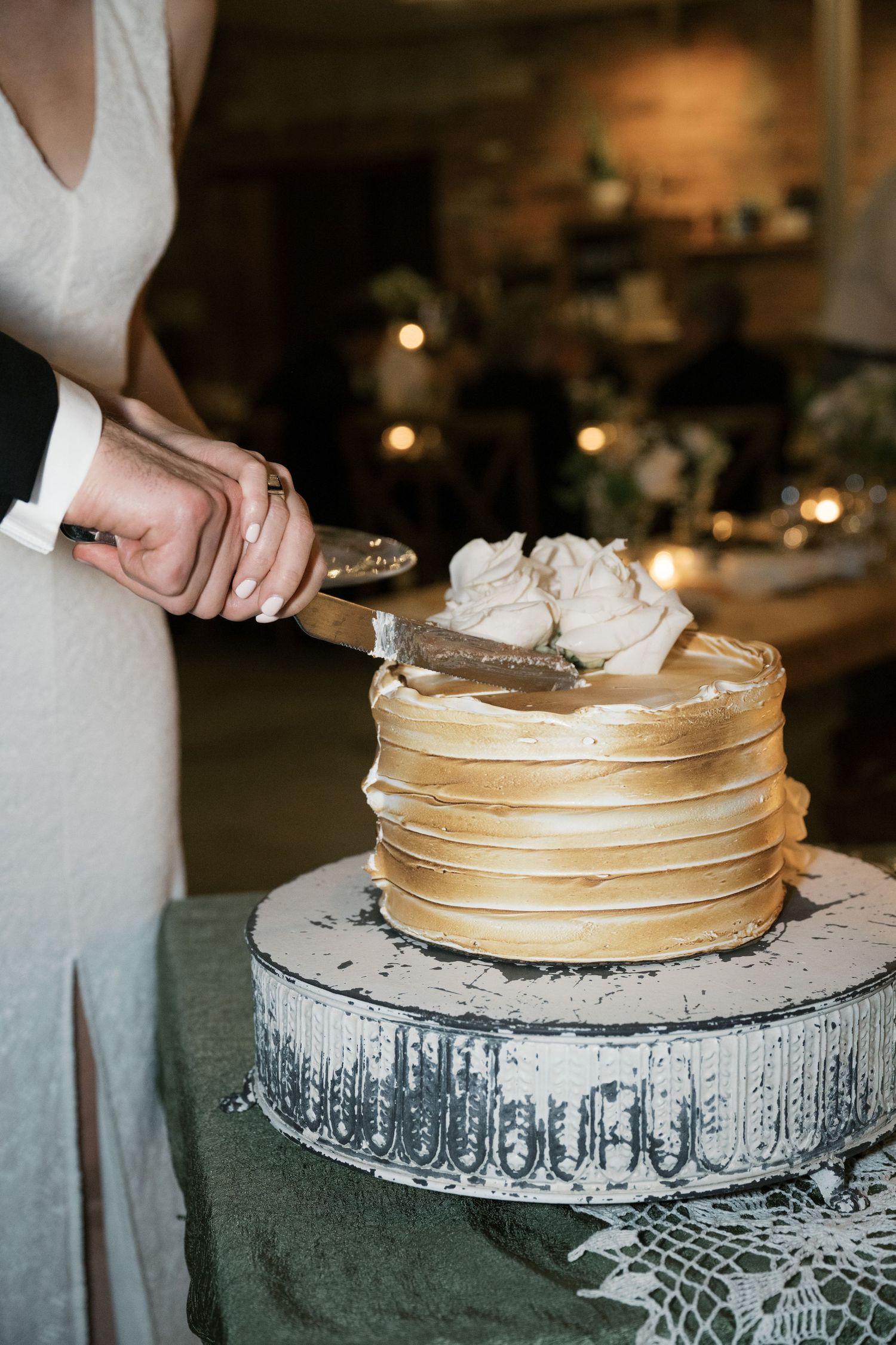 A hand cuts into a golden-colored crepe cake topped with whipped cream on an ornate silver cake stand.