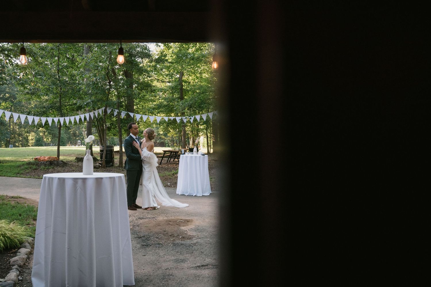 View through a doorway of an outdoor wedding ceremony with white tablecloths and bunting.