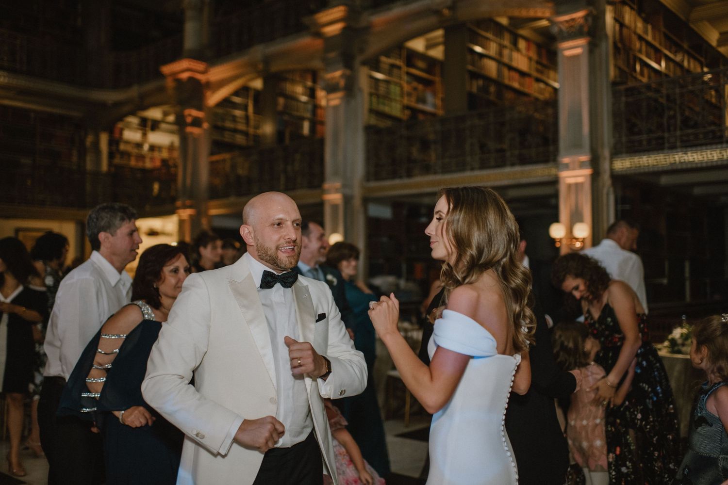 Wedding celebration in a grand library with guests dancing and celebrating in formal attire.