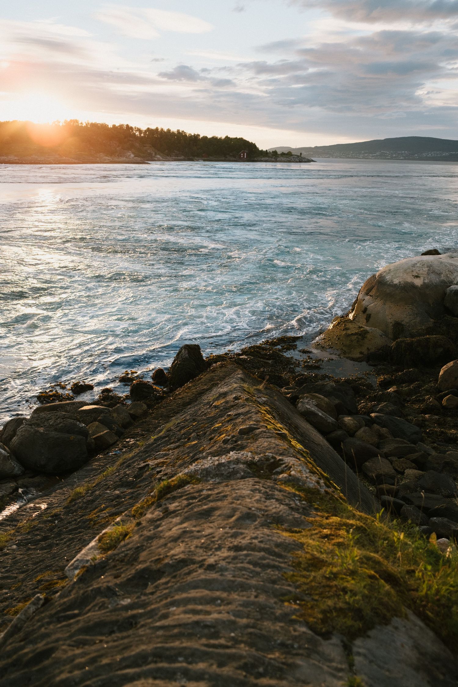 Rocky coastal shoreline at sunset with waves crashing against rugged cliffs.