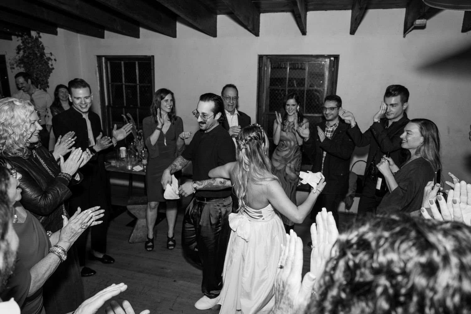 Wedding guests and couple dancing joyfully at an evening reception, captured in black and white photography.