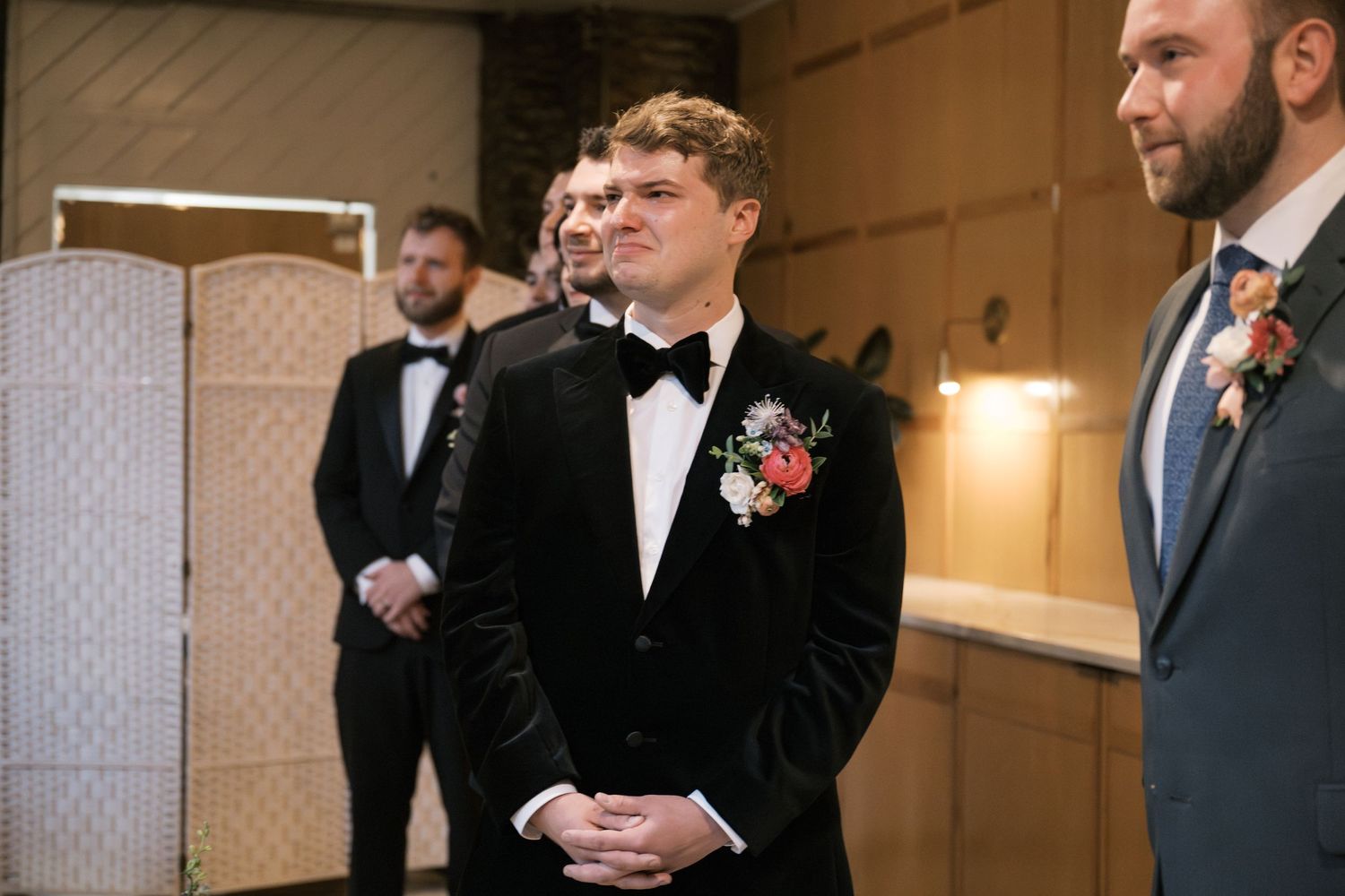 Groom in black tuxedo and bowtie stands at altar during ceremony.