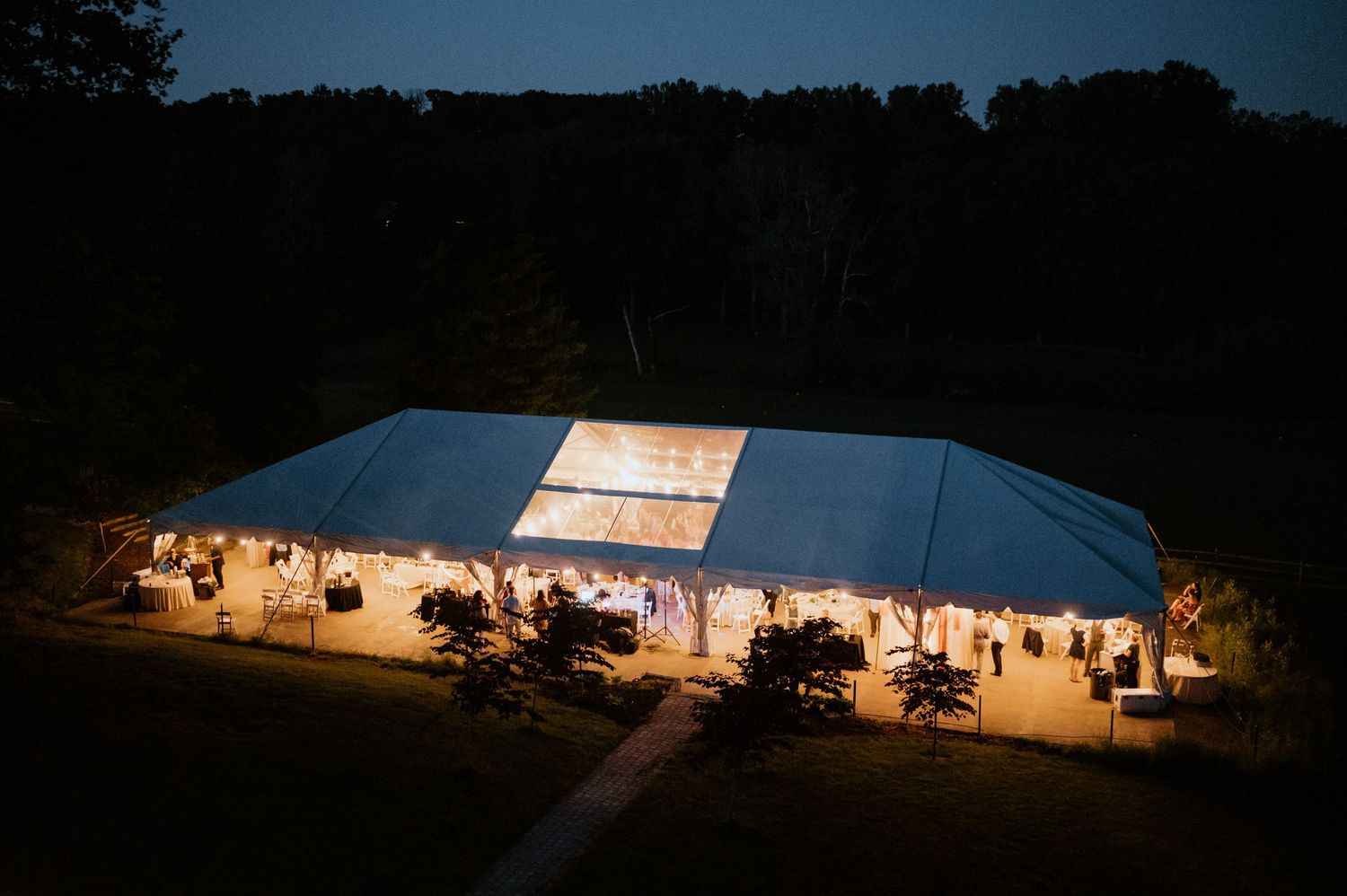 Large white wedding tent glowing at night with guests visible through the entrance.